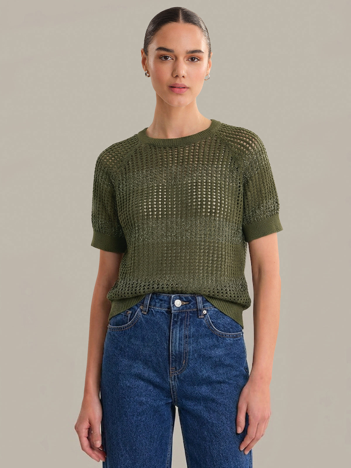 Woman wearing a green knitted top and blue jeans against a plain background