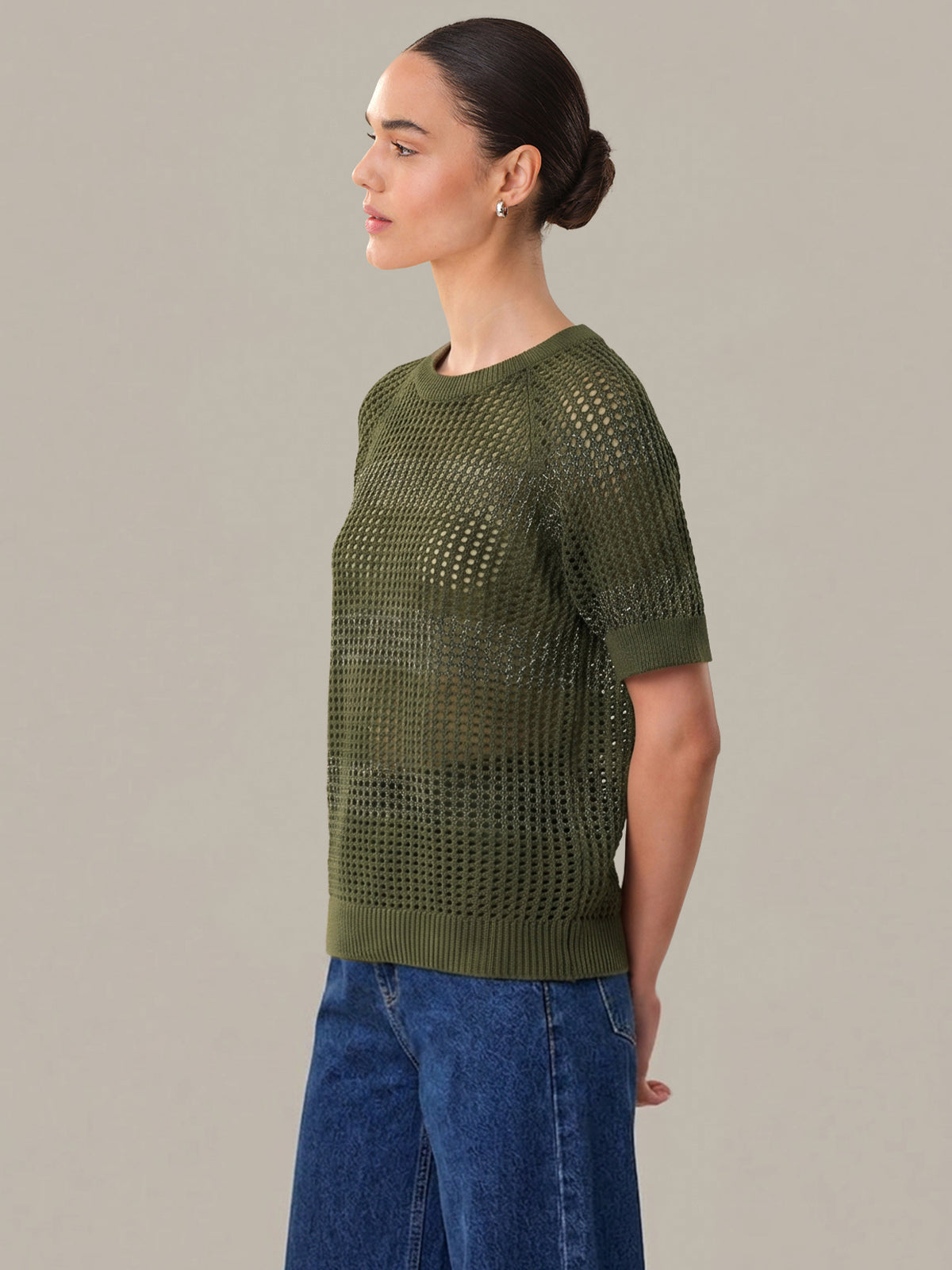 Woman wearing a green knitted sweater and blue jeans against a gray background