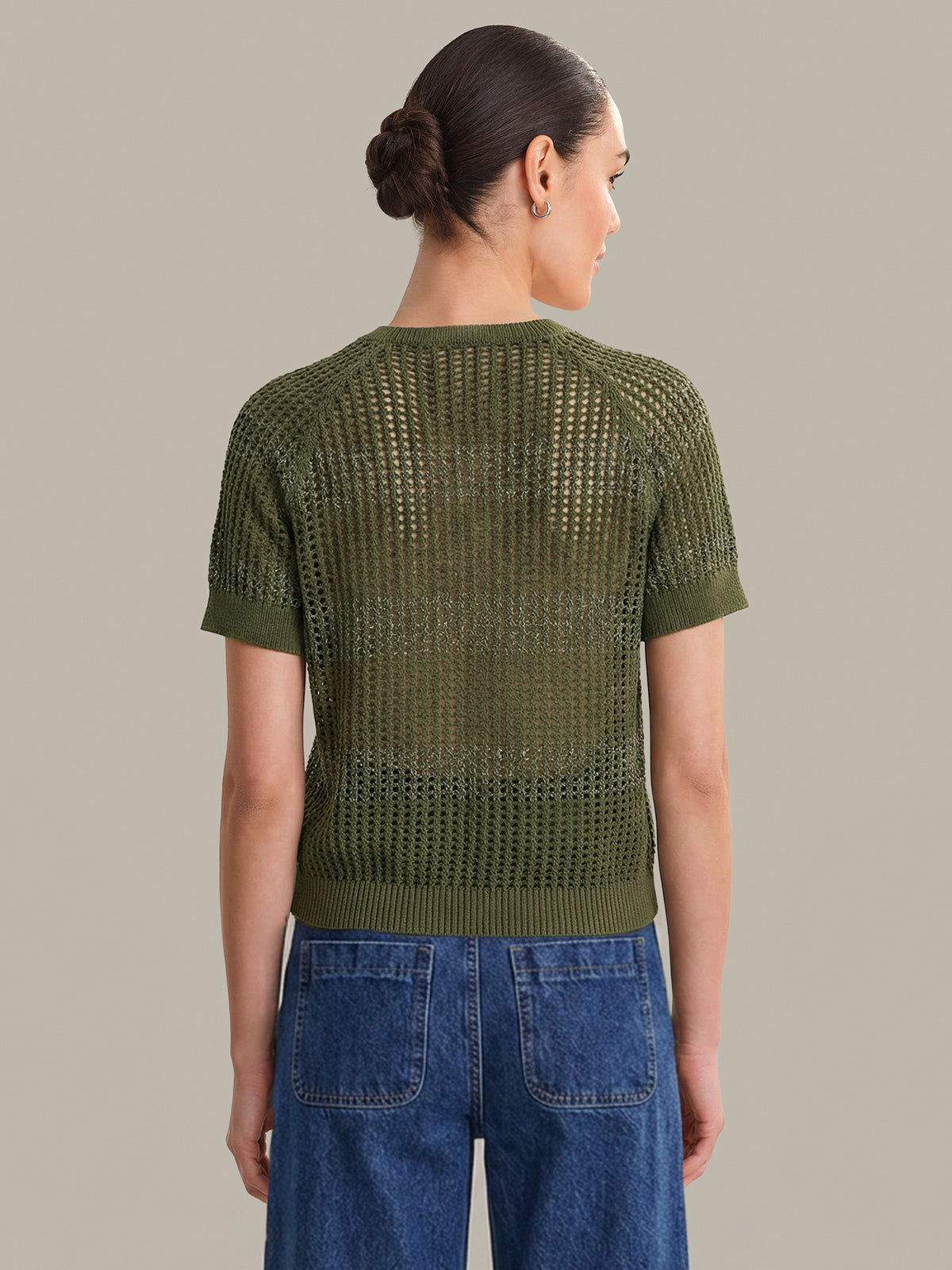 Woman wearing a green knitted top and blue jeans against a neutral background