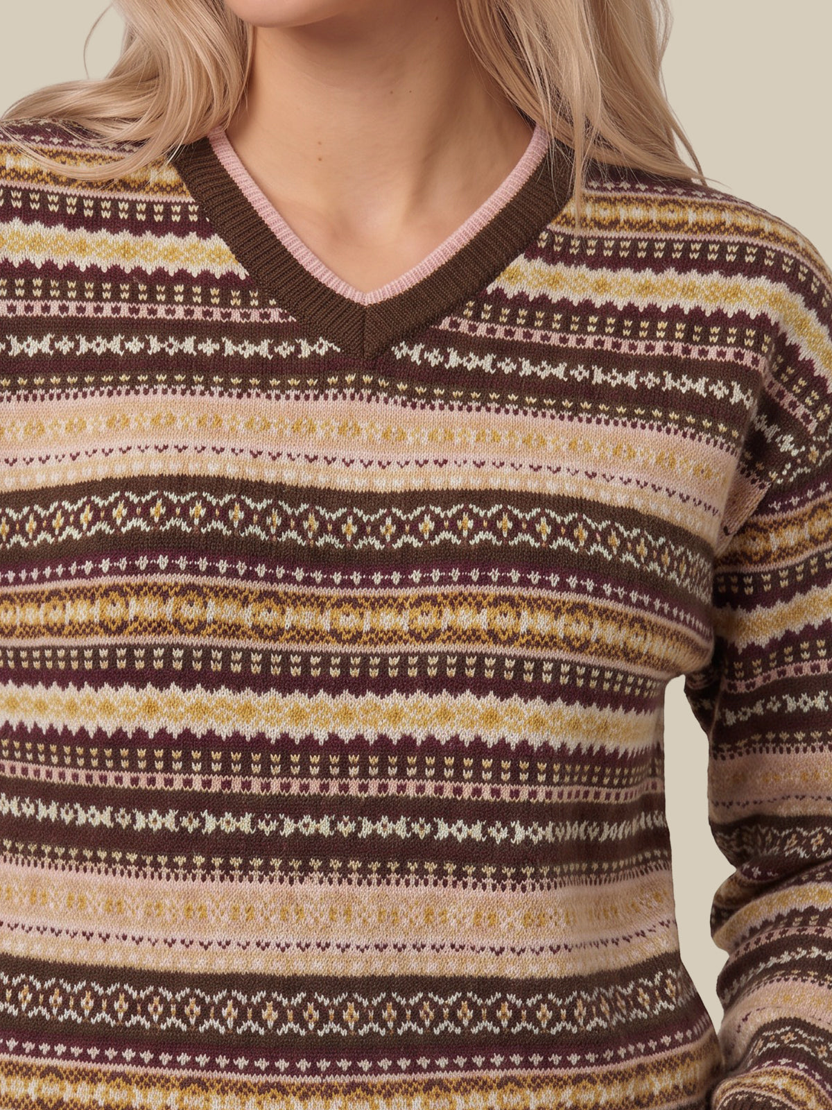 A close-up of a woman wearing a V-neck knit sweater with horizontal Fair Isle style stripes in brown, beige, cream, and muted pink.