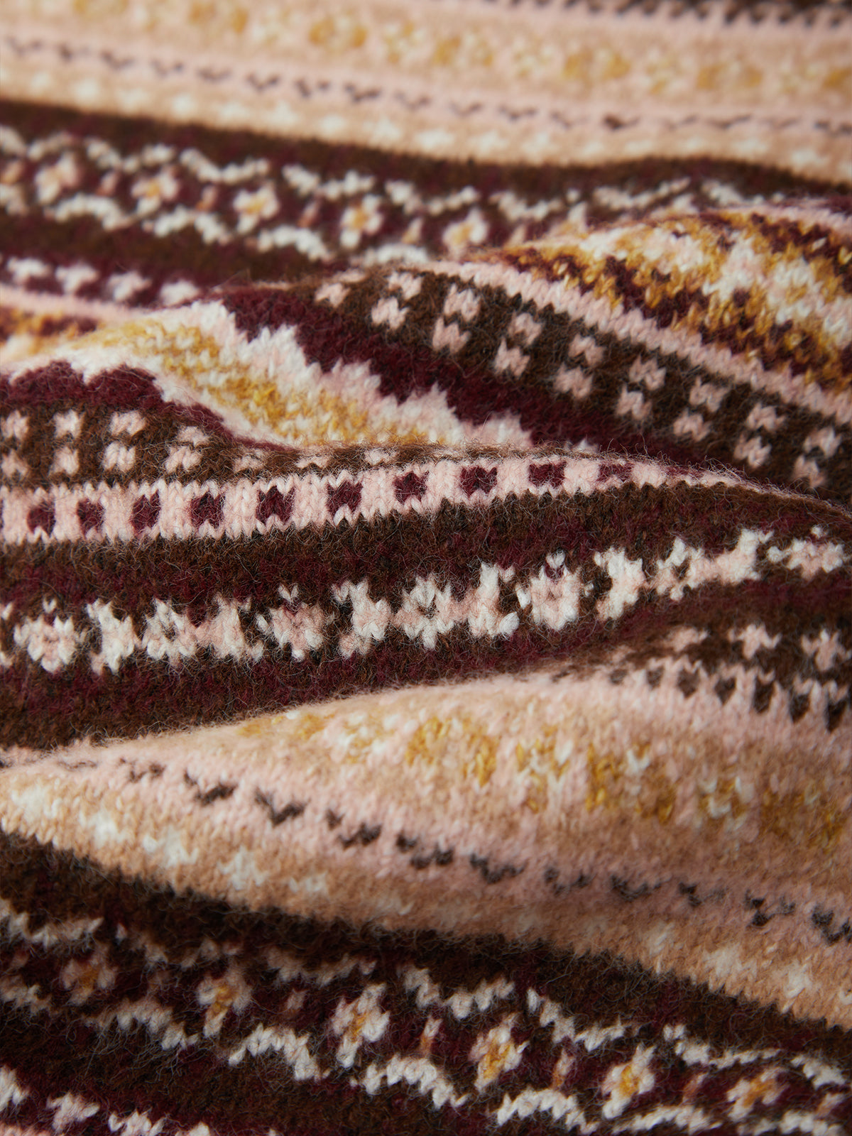 A close-up of a knitted fabric with a Fair Isle pattern in dark brown, cream, mustard yellow, and burgundy.