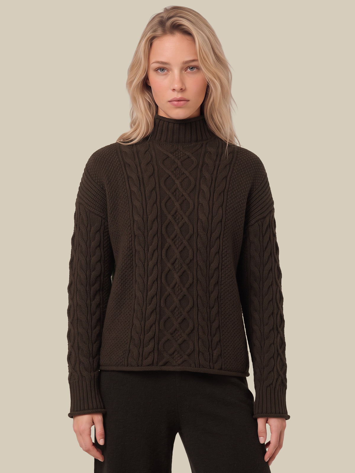 A woman modeling a dark brown cable-knit mock neck sweater against a solid beige background.