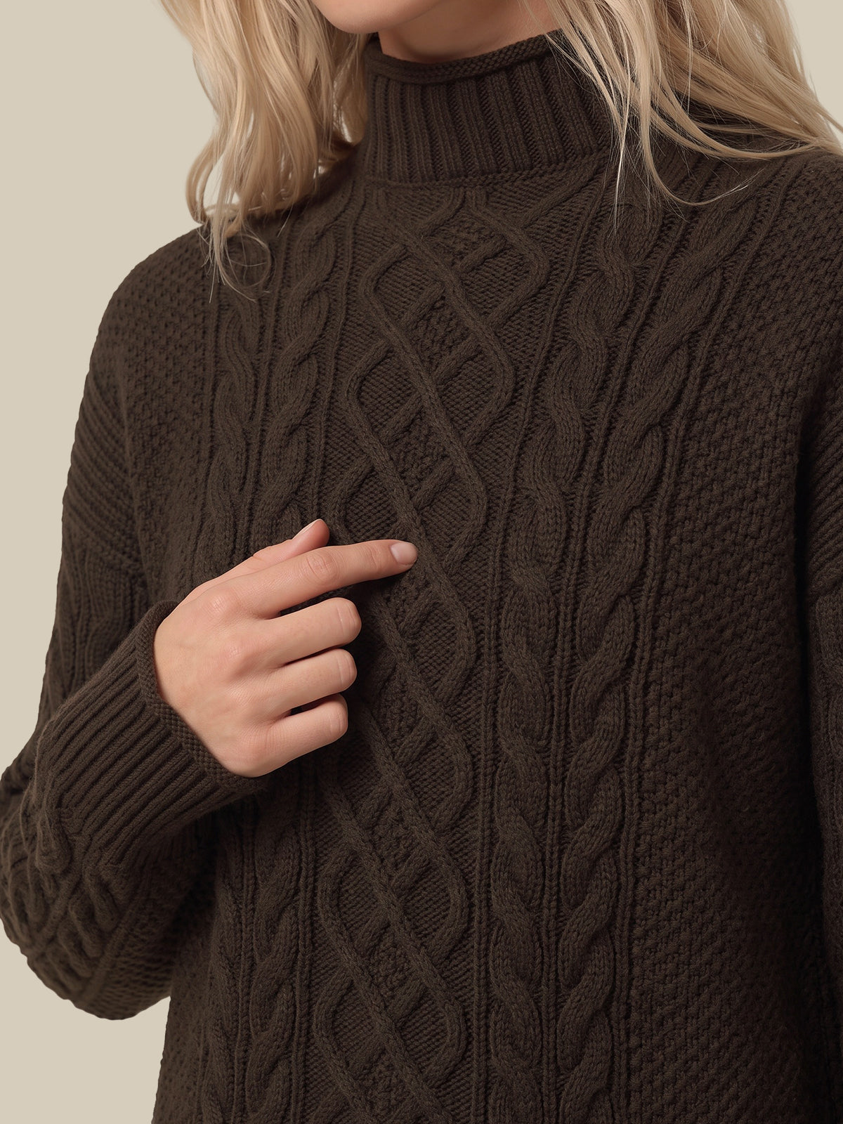 A close-up of a person wearing a dark brown cable-knit mock-neck sweater, with a hand pointing toward the knit texture.