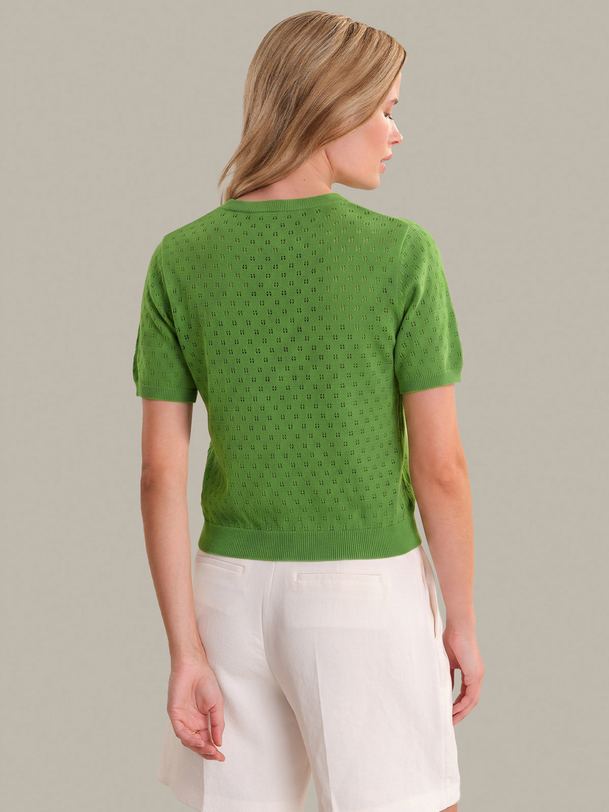 Woman wearing a green patterned shirt and white pants on a plain background