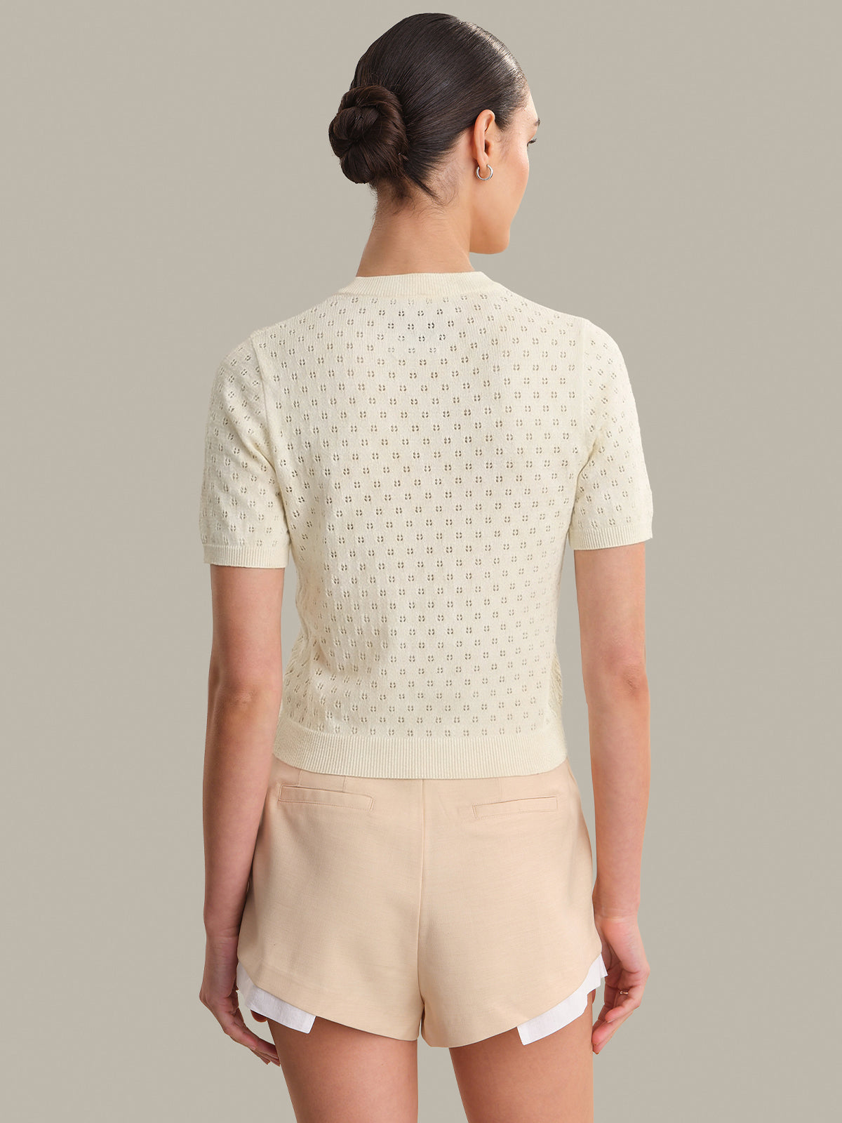 Woman wearing a light-colored top and beige shorts against a neutral background