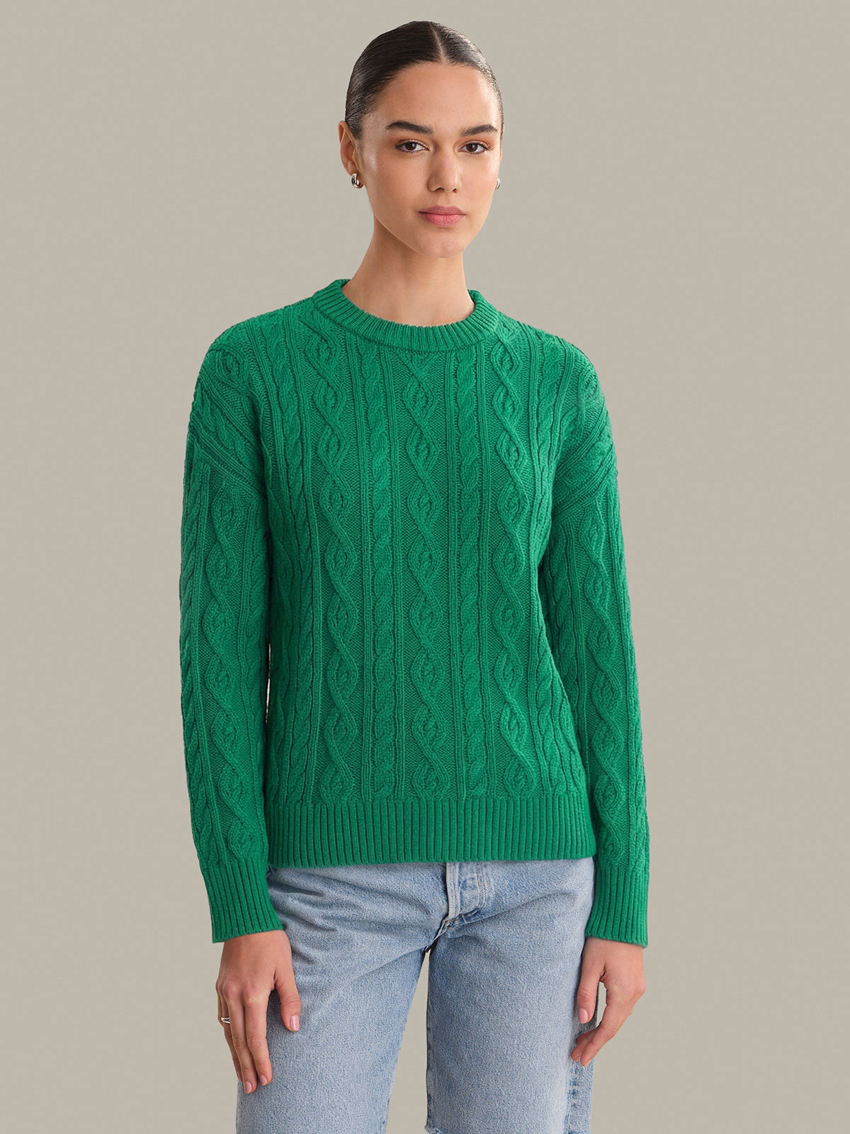 Person wearing a green cable knit sweater against a neutral background