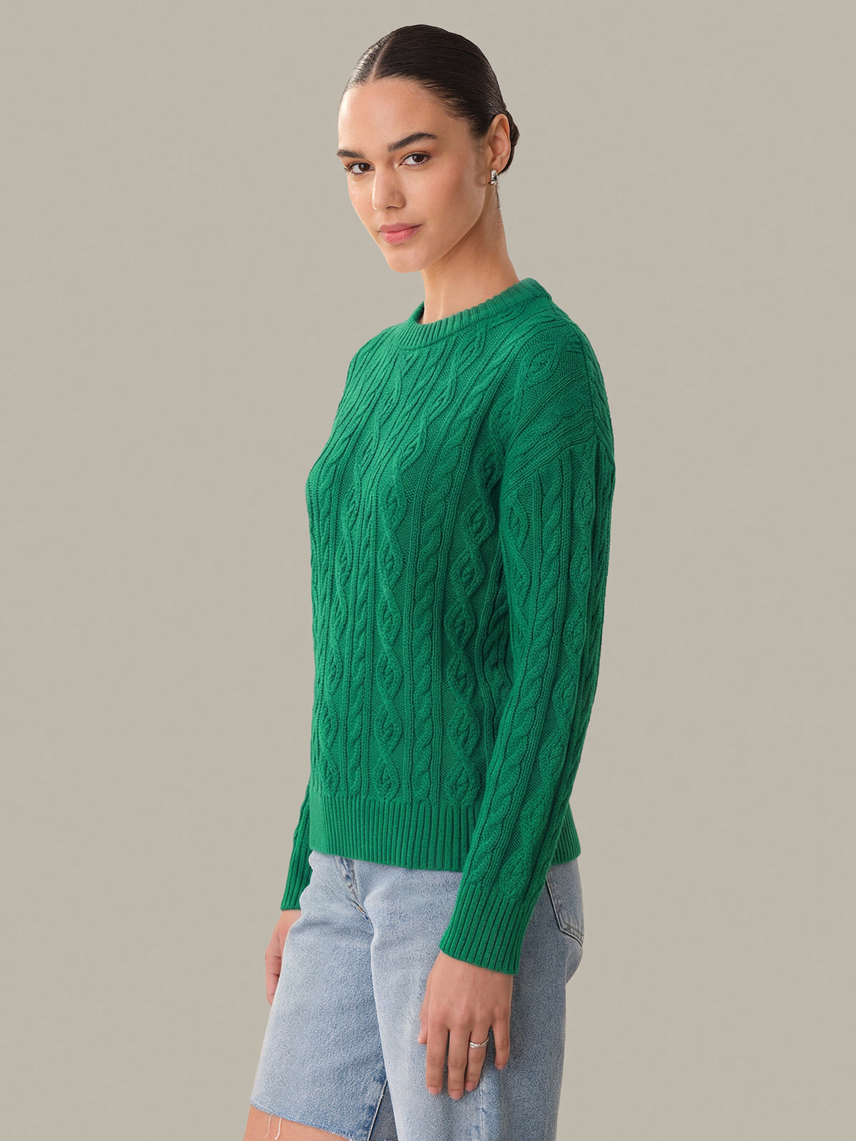 Woman wearing a green cable knit sweater against a plain background