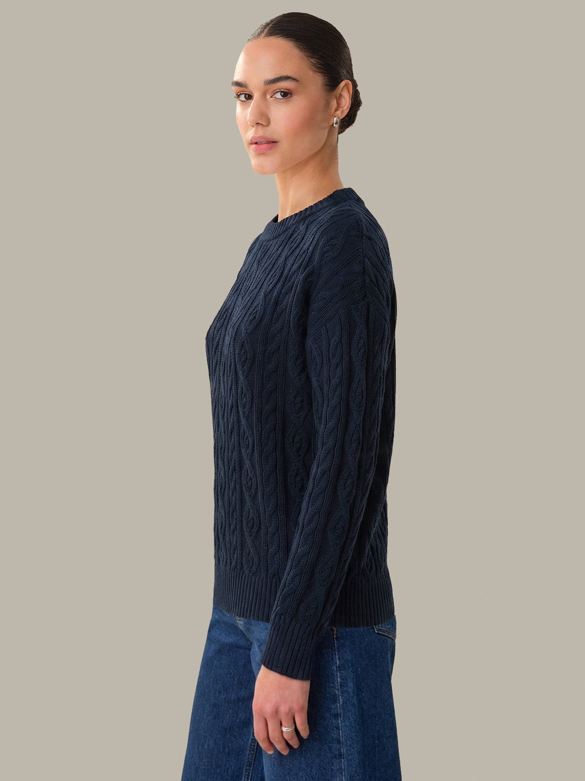 Woman wearing a dark blue cable knit sweater against a plain background