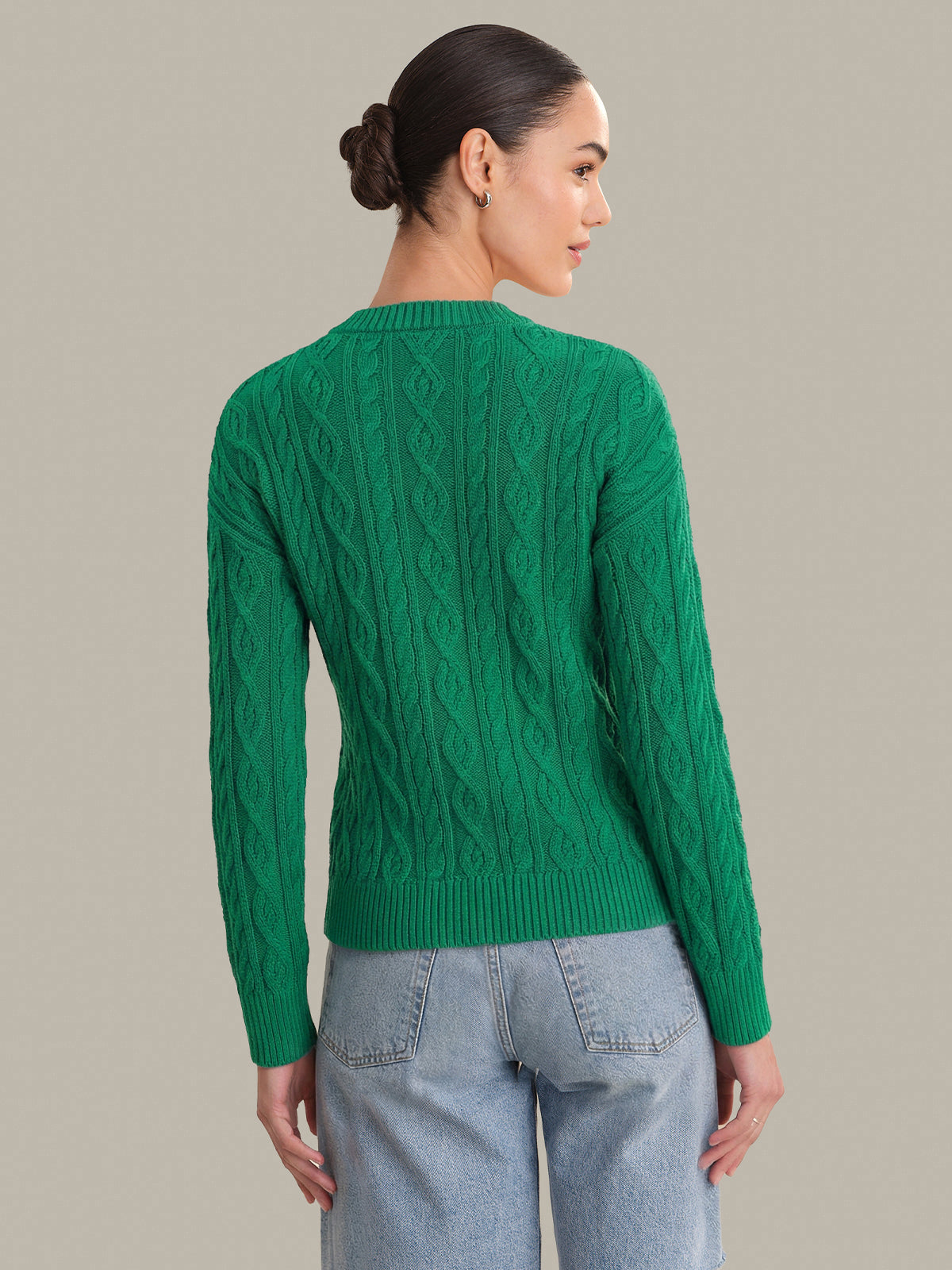 Woman wearing a green cable knit sweater against a neutral background