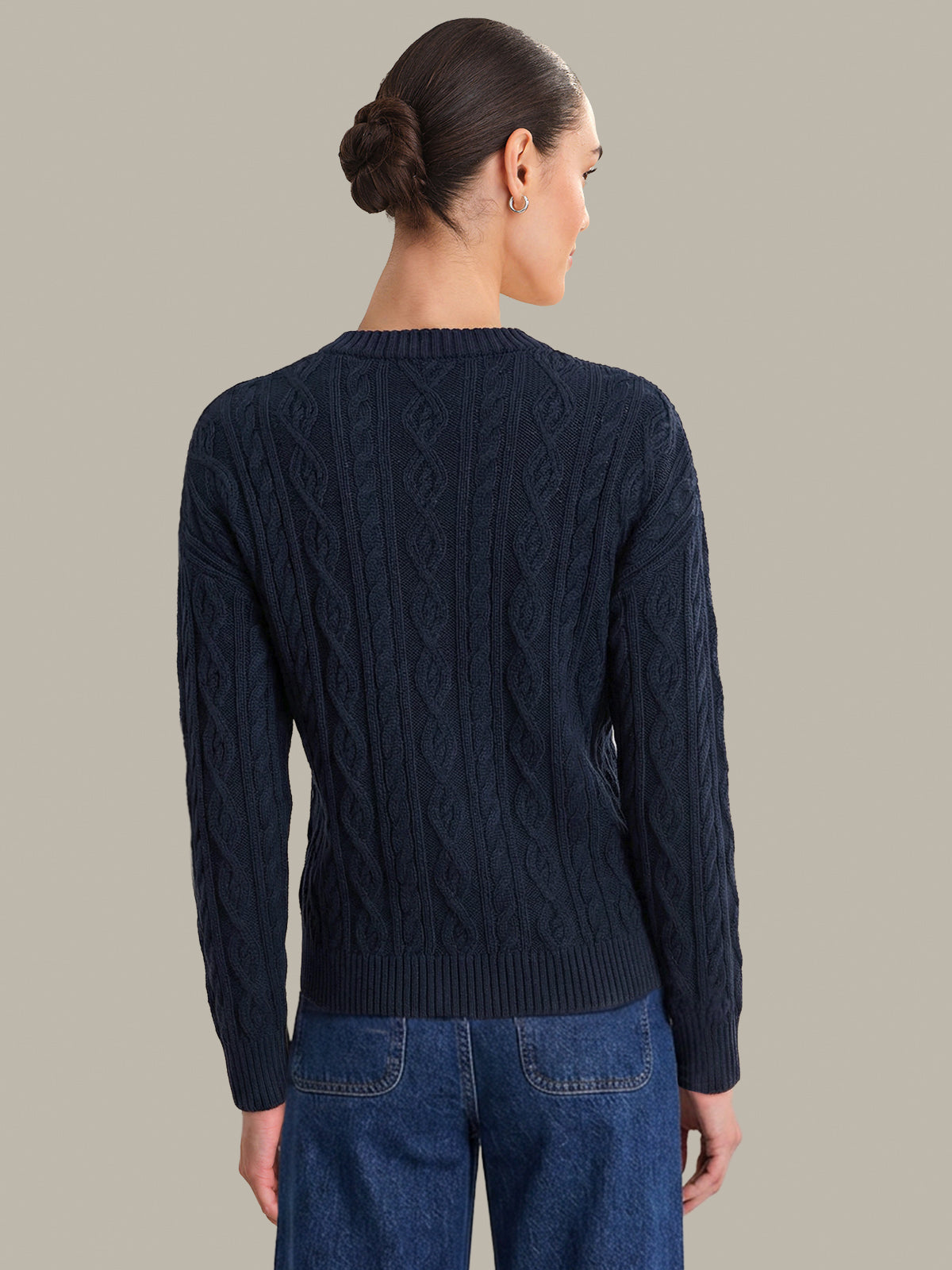 Woman wearing a dark blue cable knit sweater against a plain background