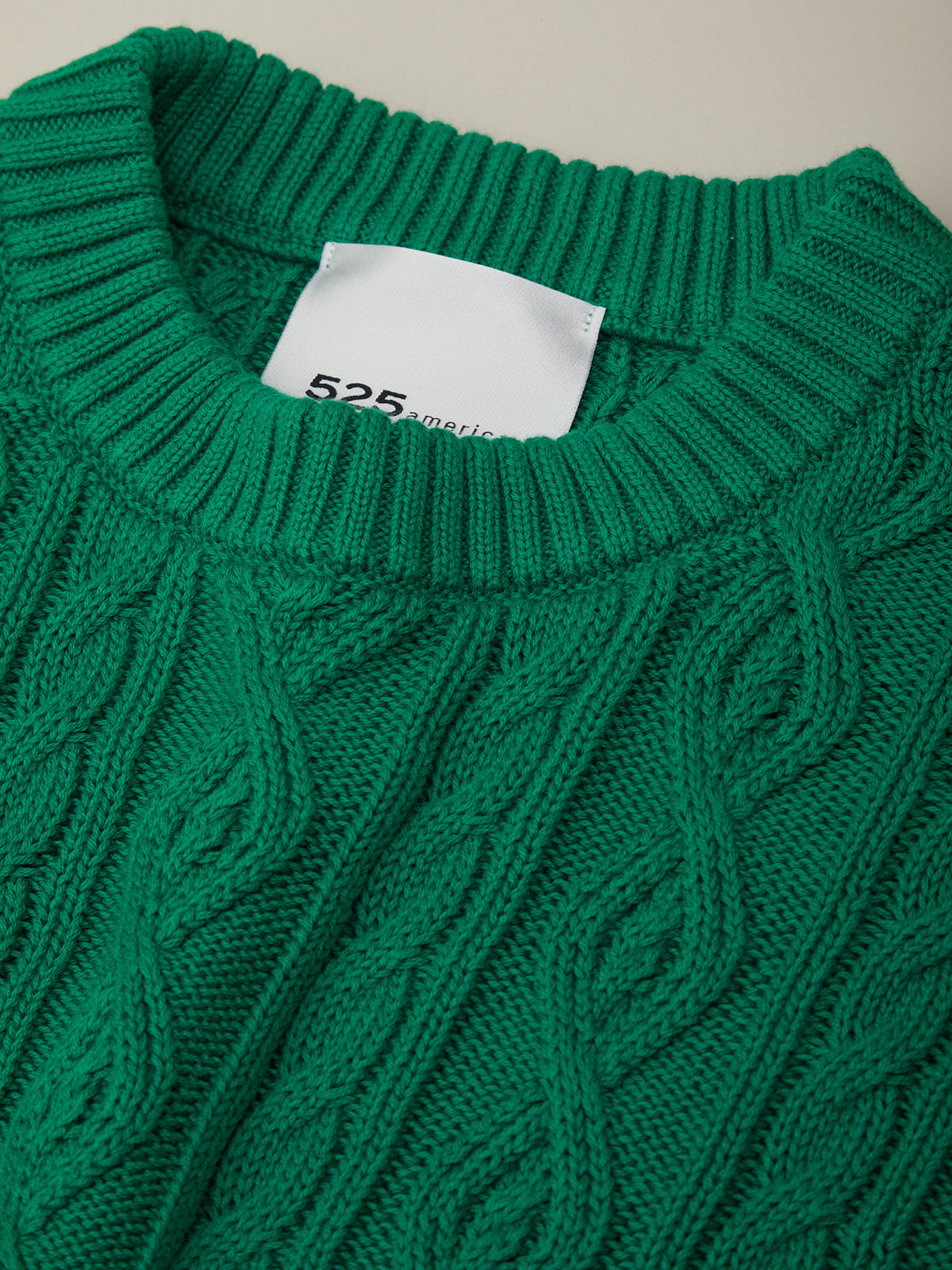Close-up of a green cable knit sweater with a brand label.