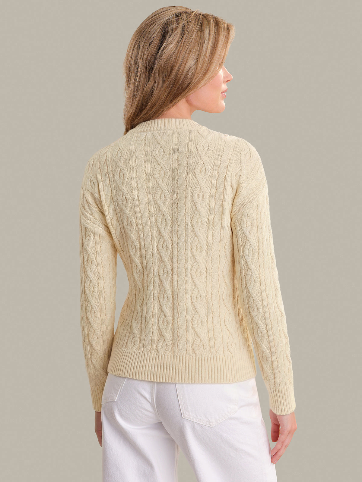 Woman wearing a beige cable knit sweater against a plain background