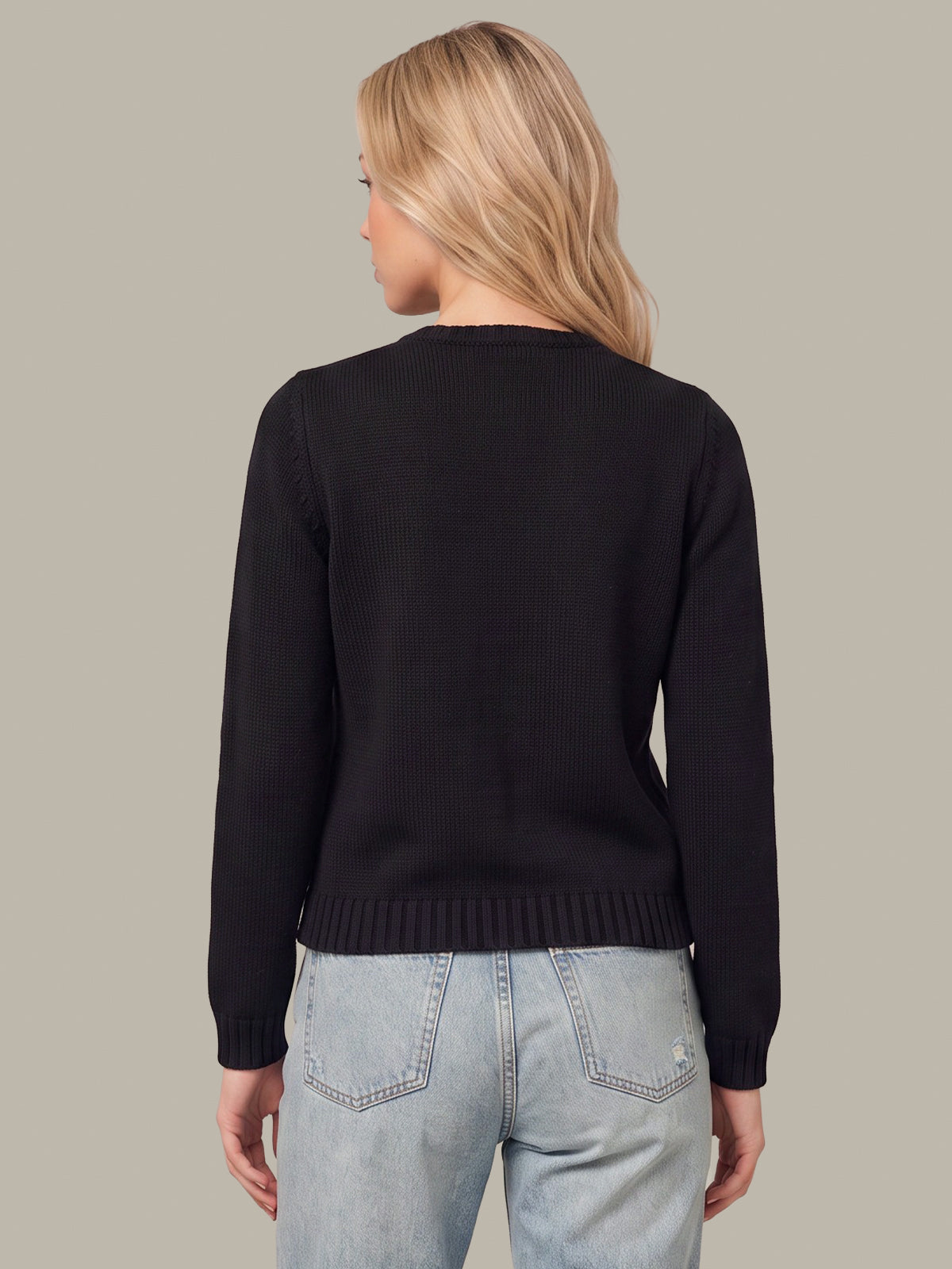 A woman shown from the back wearing a black long-sleeve knit sweater and light blue jeans against a solid taupe background.