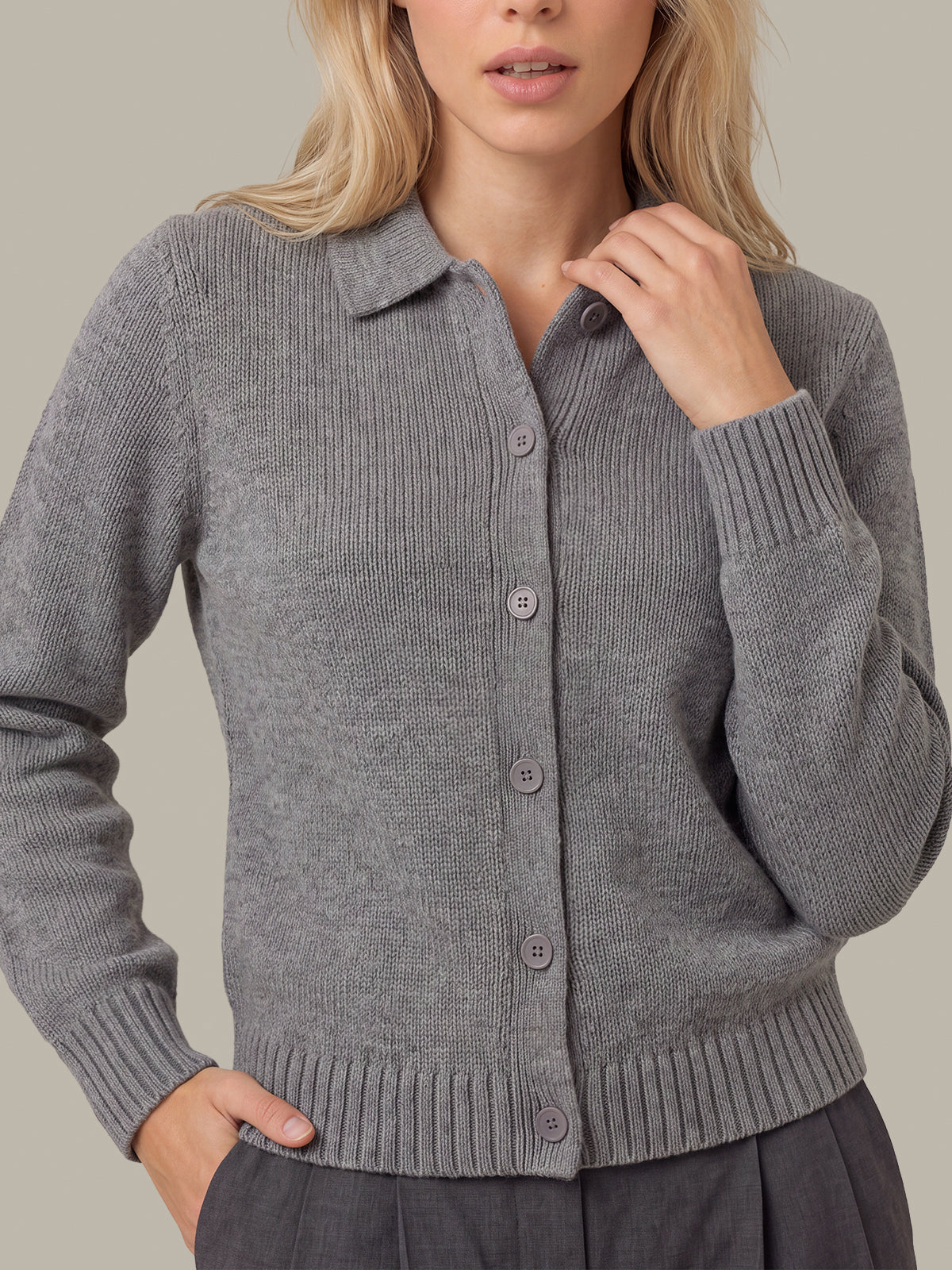 A woman wearing a gray ribbed knit cardigan sweater with a button-front closure and collar, shown against a plain warm beige background.