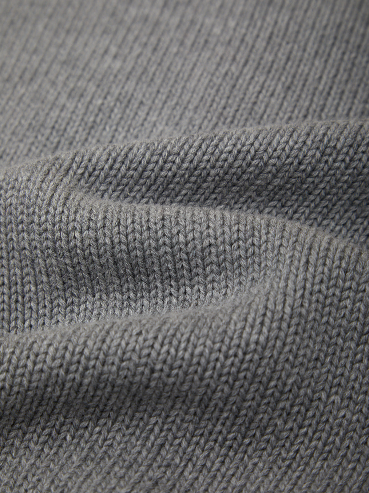 Close-up of a gray knit fabric texture with soft folds showing the ribbed weave pattern.