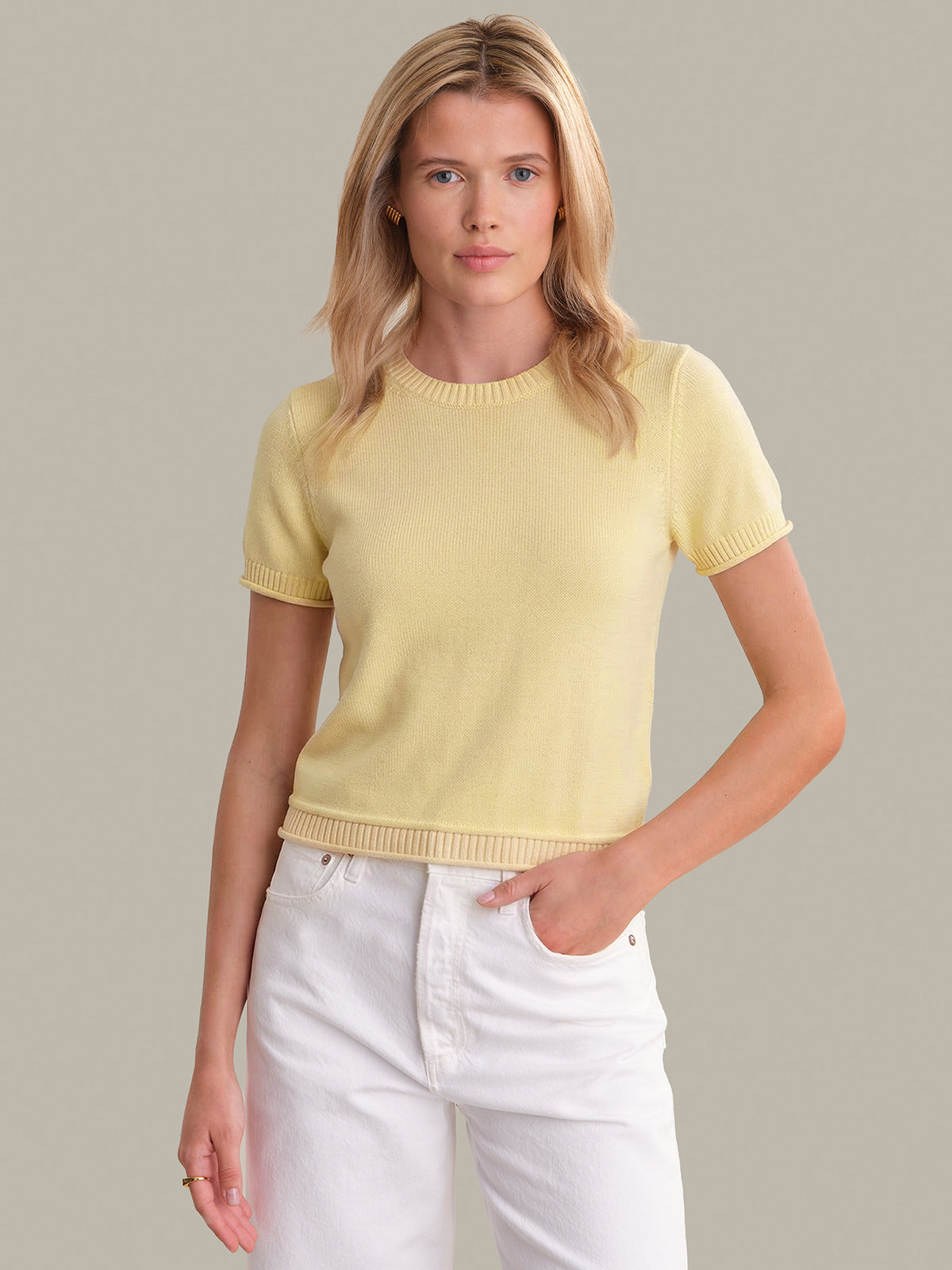 Woman wearing a yellow sweater and white pants against a neutral background