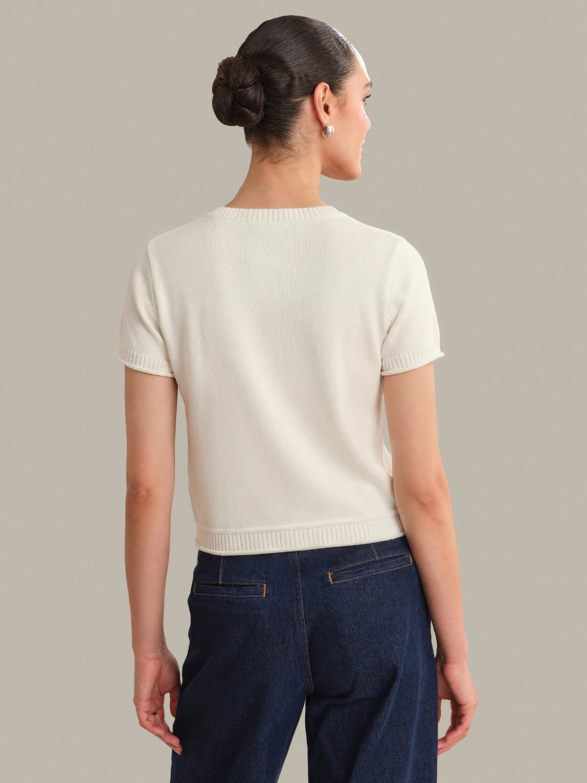 Woman wearing a white short-sleeve sweater and dark blue pants on a plain background