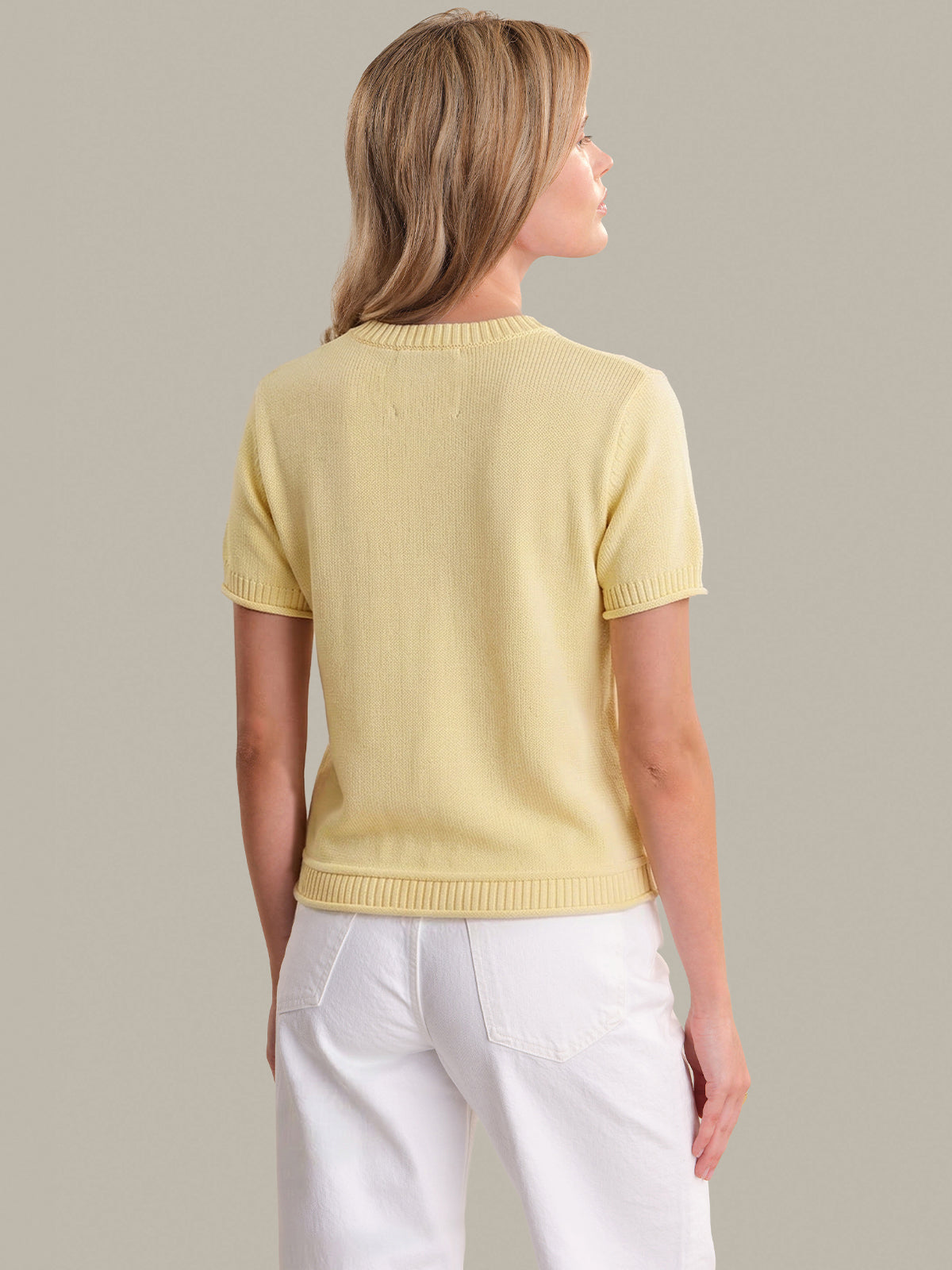 Woman wearing a yellow sweater and white pants against a plain background