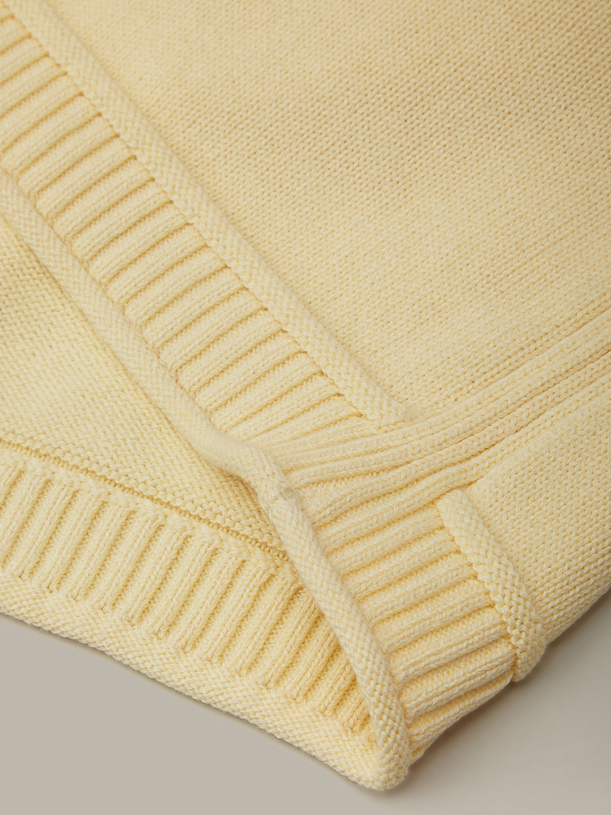 Close-up of a folded beige knitted blanket on a neutral background