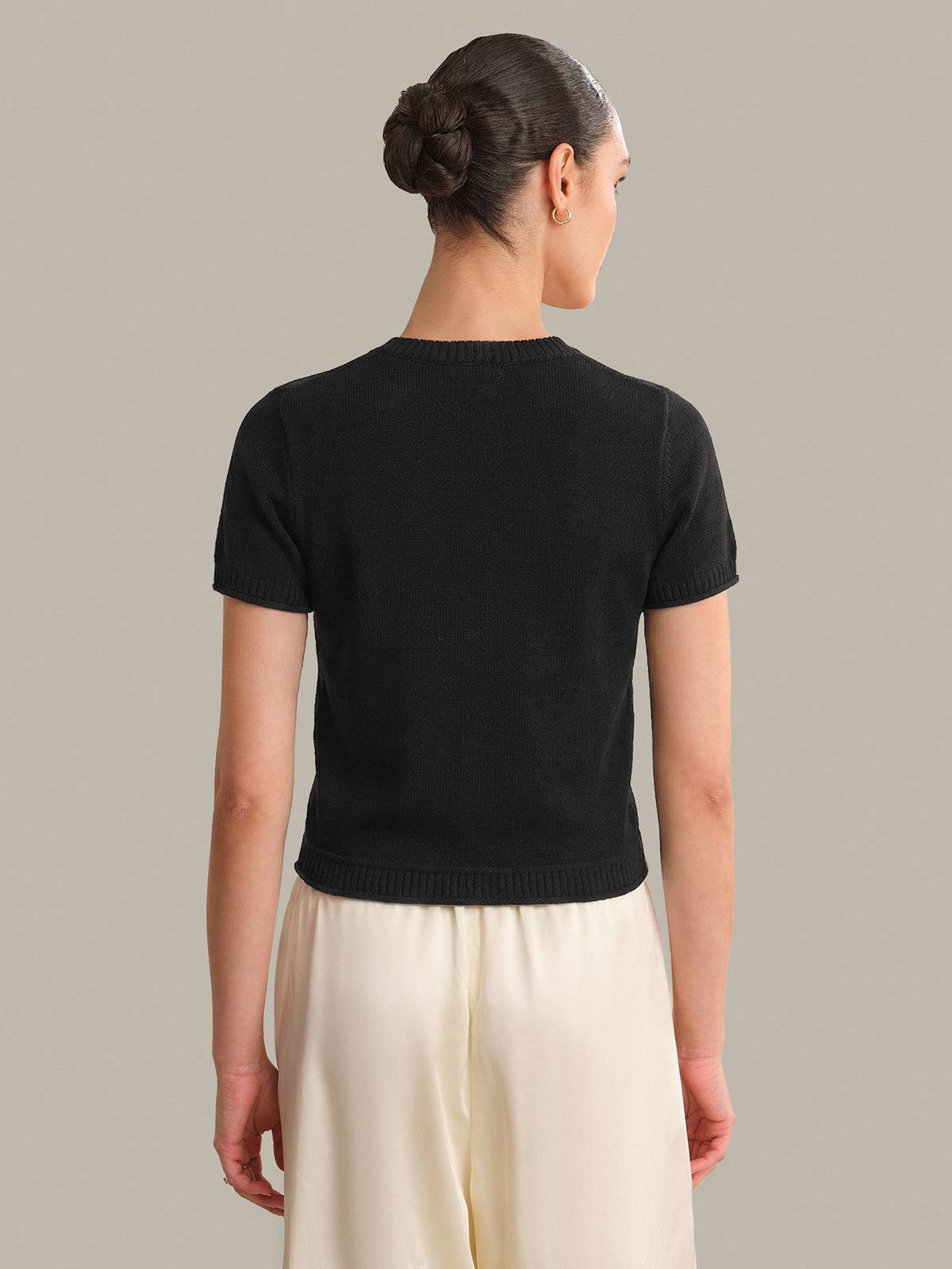 Person wearing a black short-sleeve top and beige pants on a plain background
