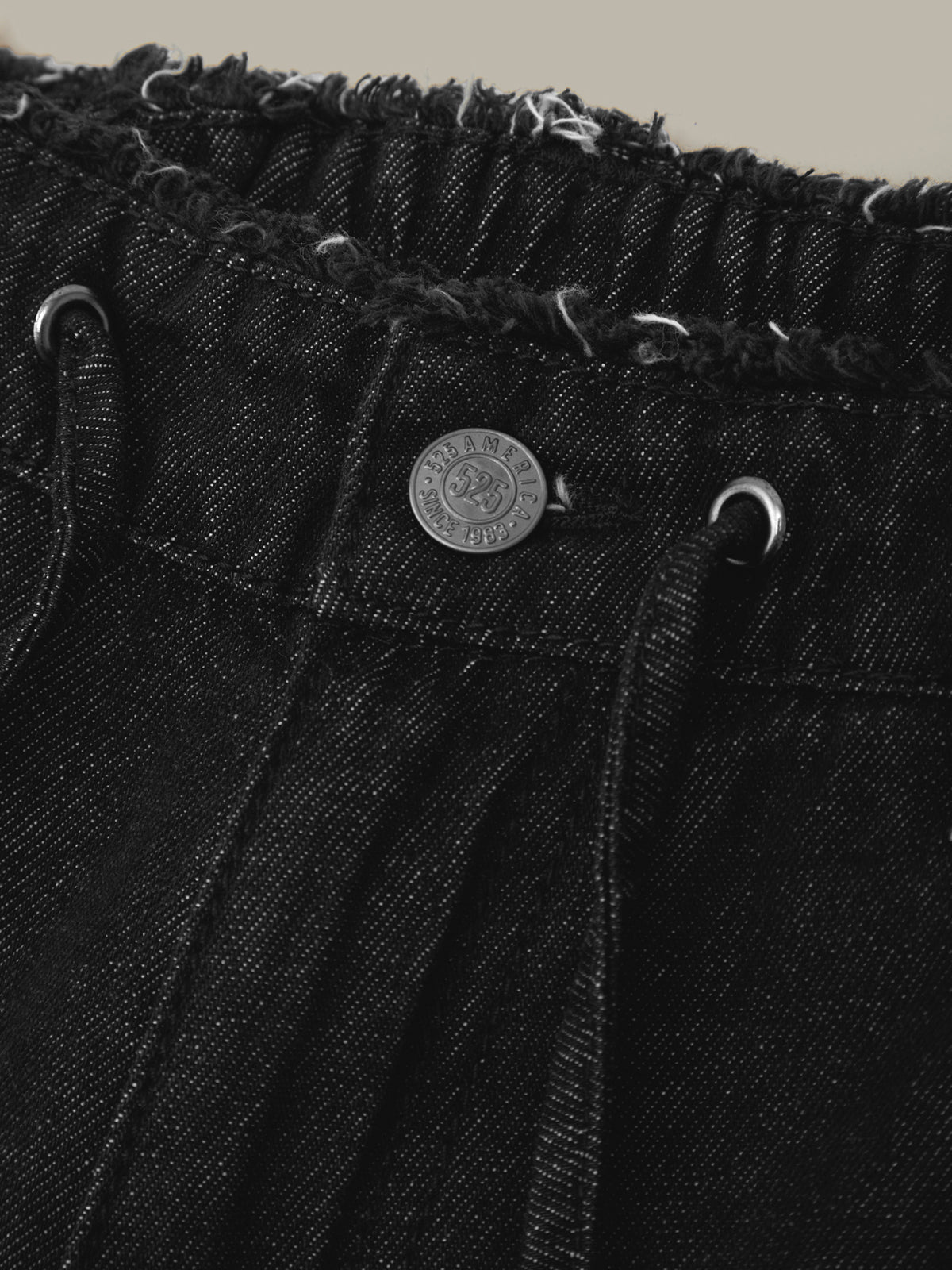 Close-up of a black denim jacket with a brand logo on the chest pocket against a beige background.