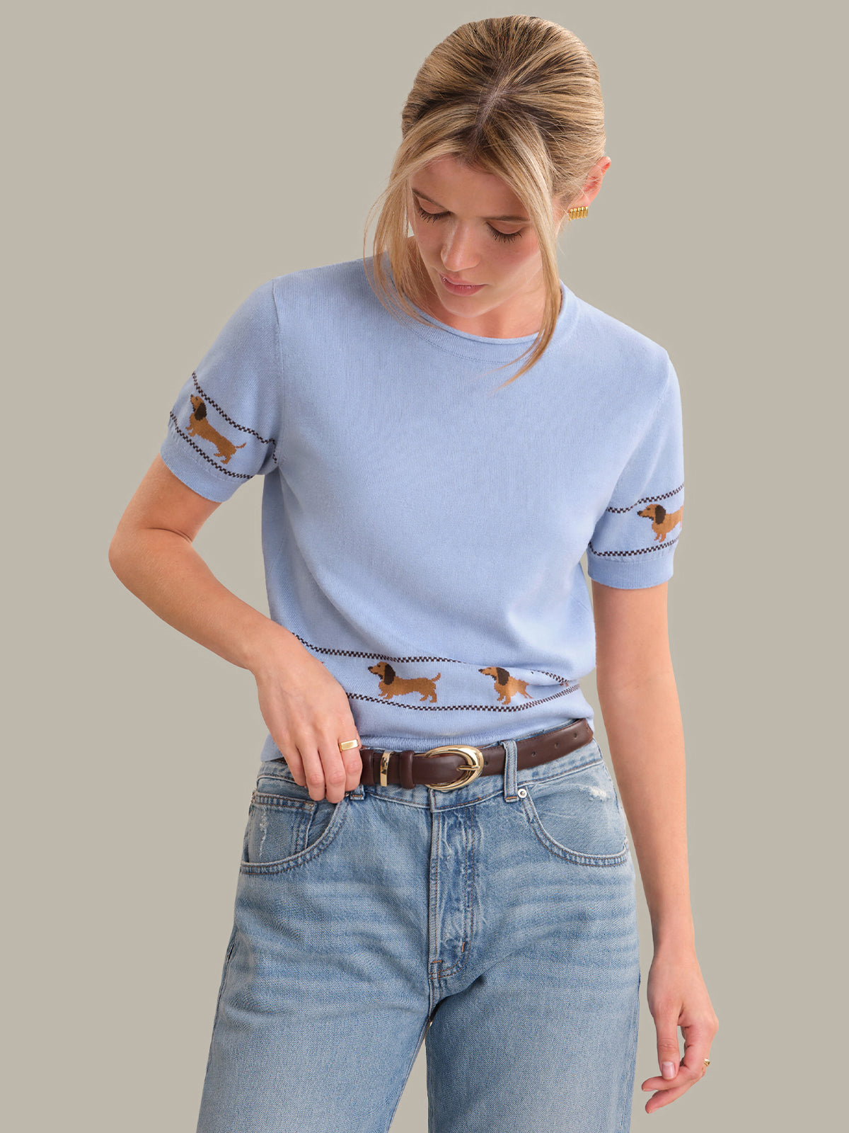 Woman wearing a light blue sweater with dachshund patterns and high-waisted jeans on a plain background