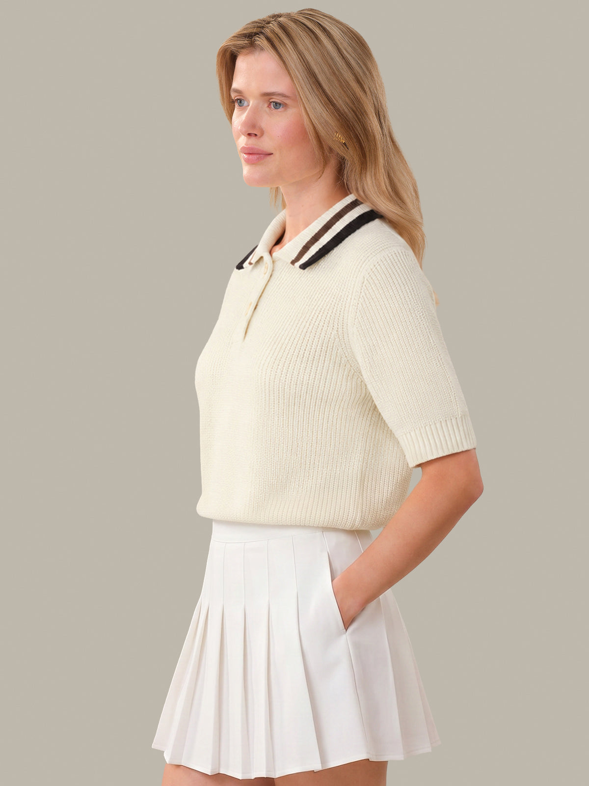 Woman wearing a cream-colored outfit with a polo shirt and pleated skirt on a plain background