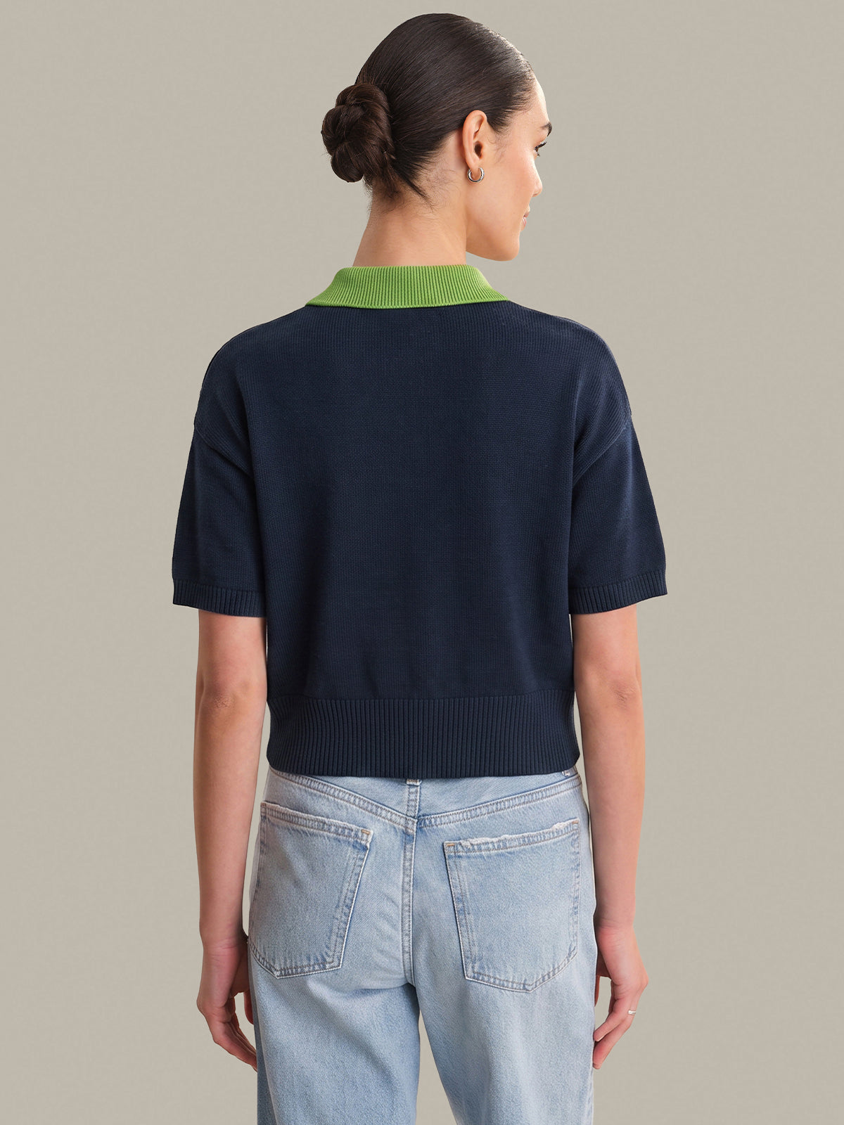 Person wearing a navy sweater with green trim and light blue jeans on a neutral background