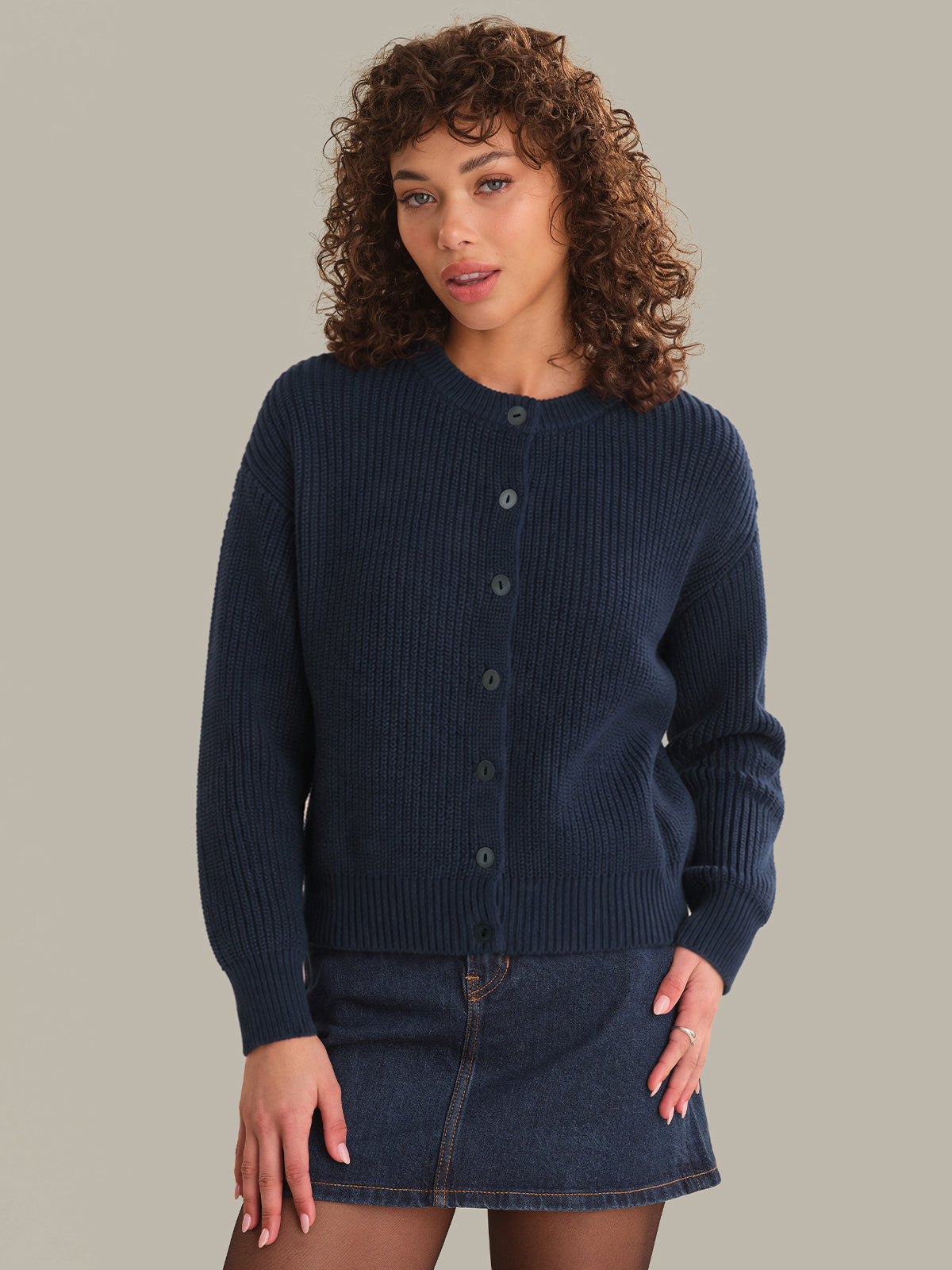 Woman wearing a navy blue cardigan and denim skirt against a neutral background