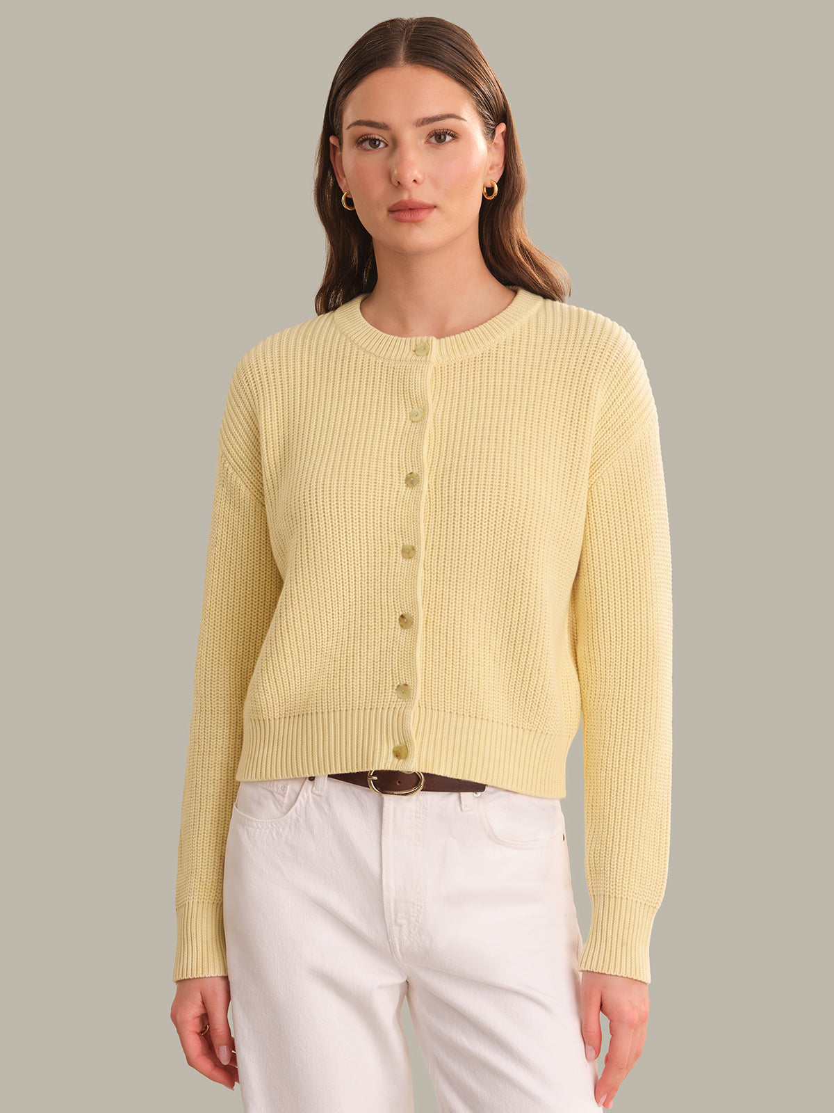Woman wearing a light yellow ribbed cardigan against a gray background