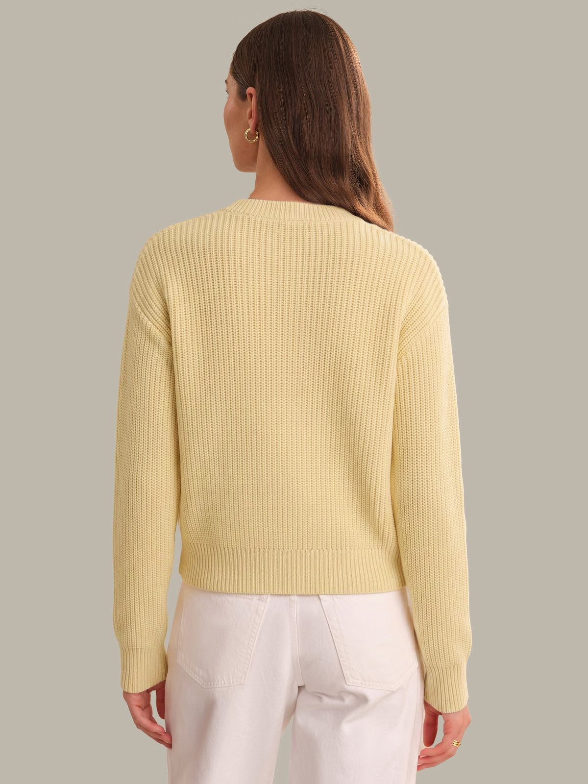 Woman wearing a light yellow ribbed sweater against a neutral background