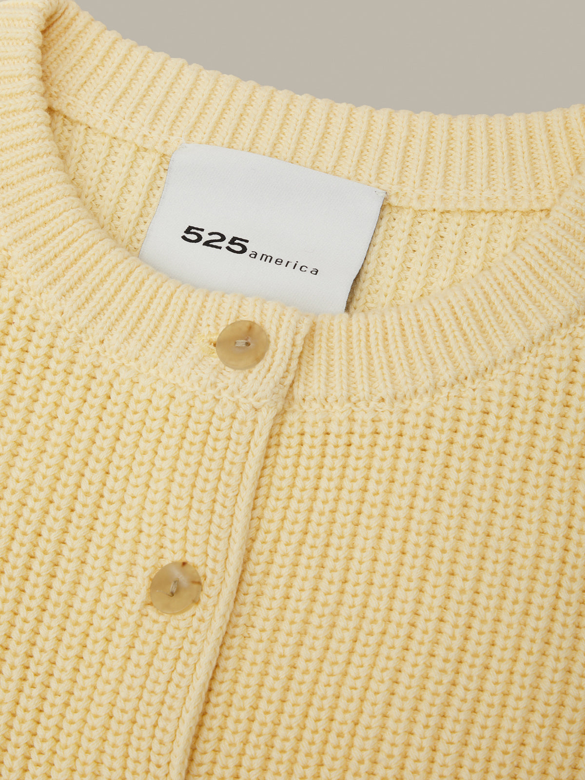 Close-up of a yellow textured garment with a brand label on a neutral background