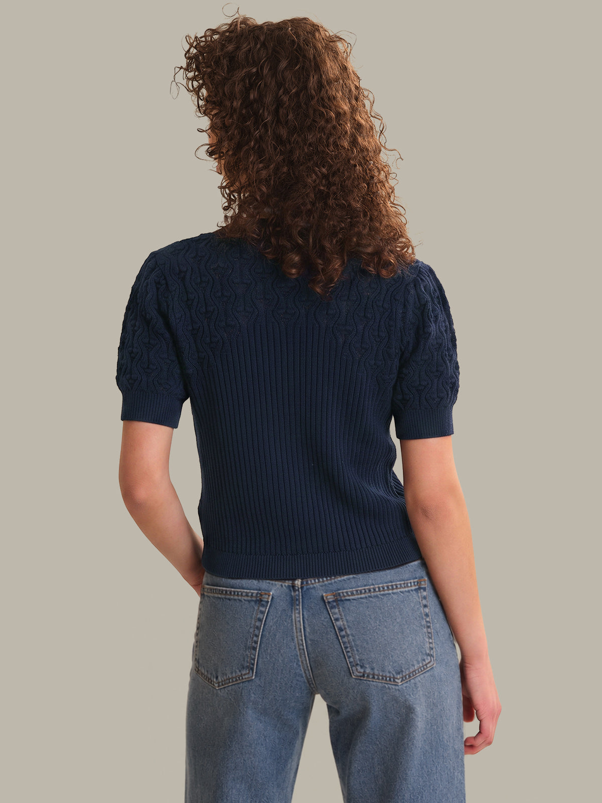 Person wearing a navy blue sweater and blue jeans on a plain background
