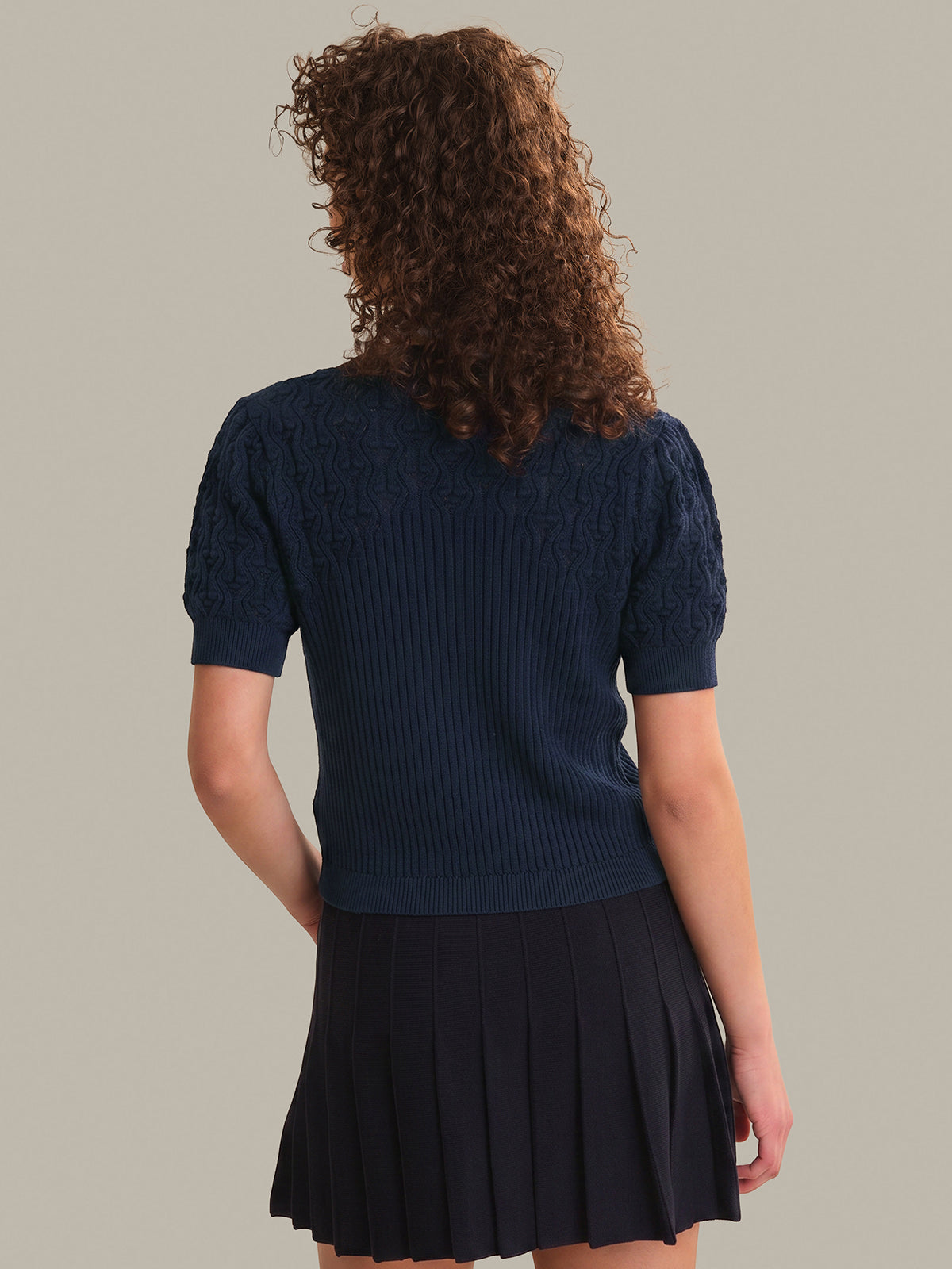 Person wearing a navy blue sweater and pleated skirt on a plain background