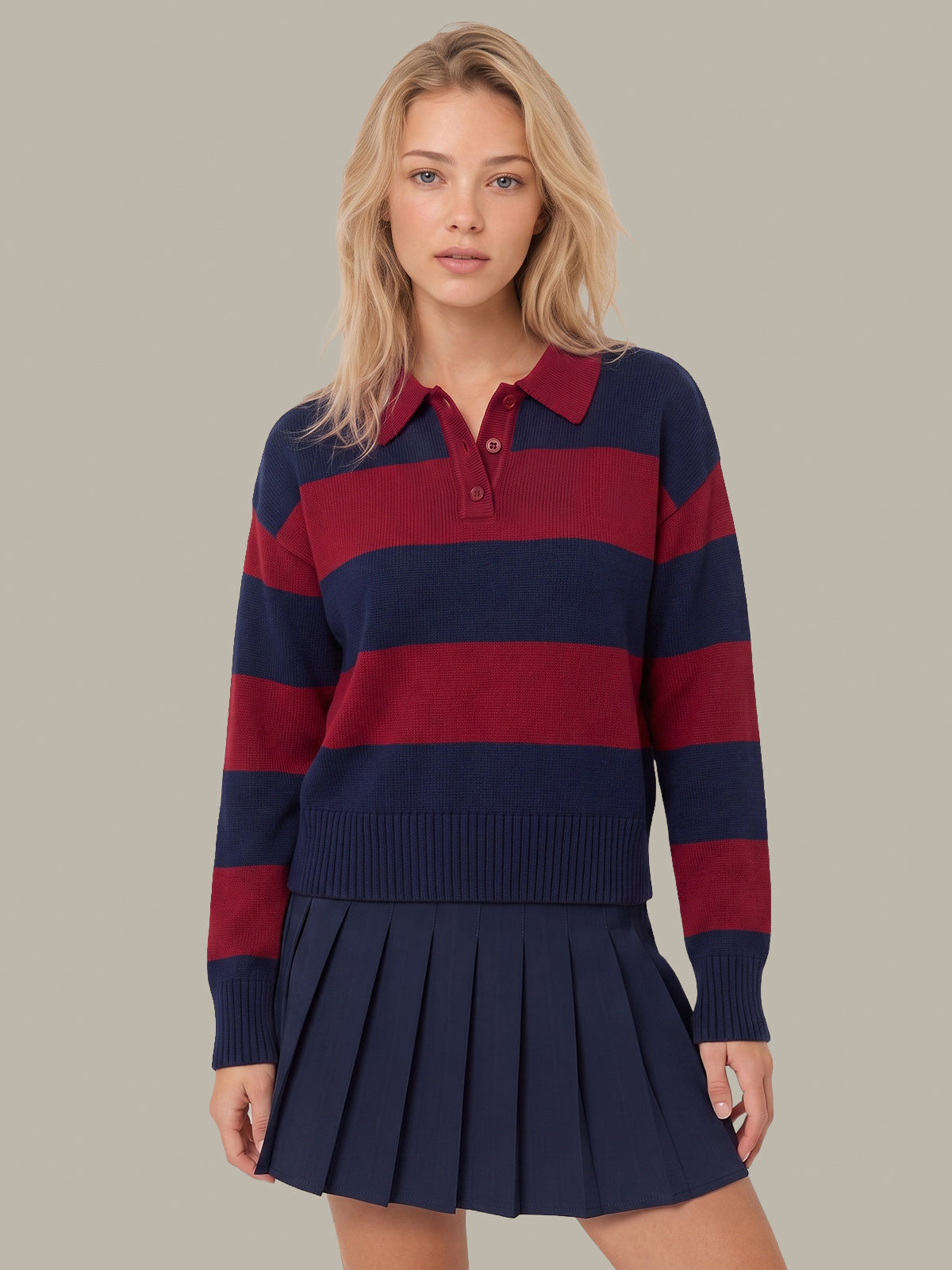 A woman modeling a navy and burgundy striped knit polo sweater with a matching pleated navy mini skirt, set against a solid beige background.
