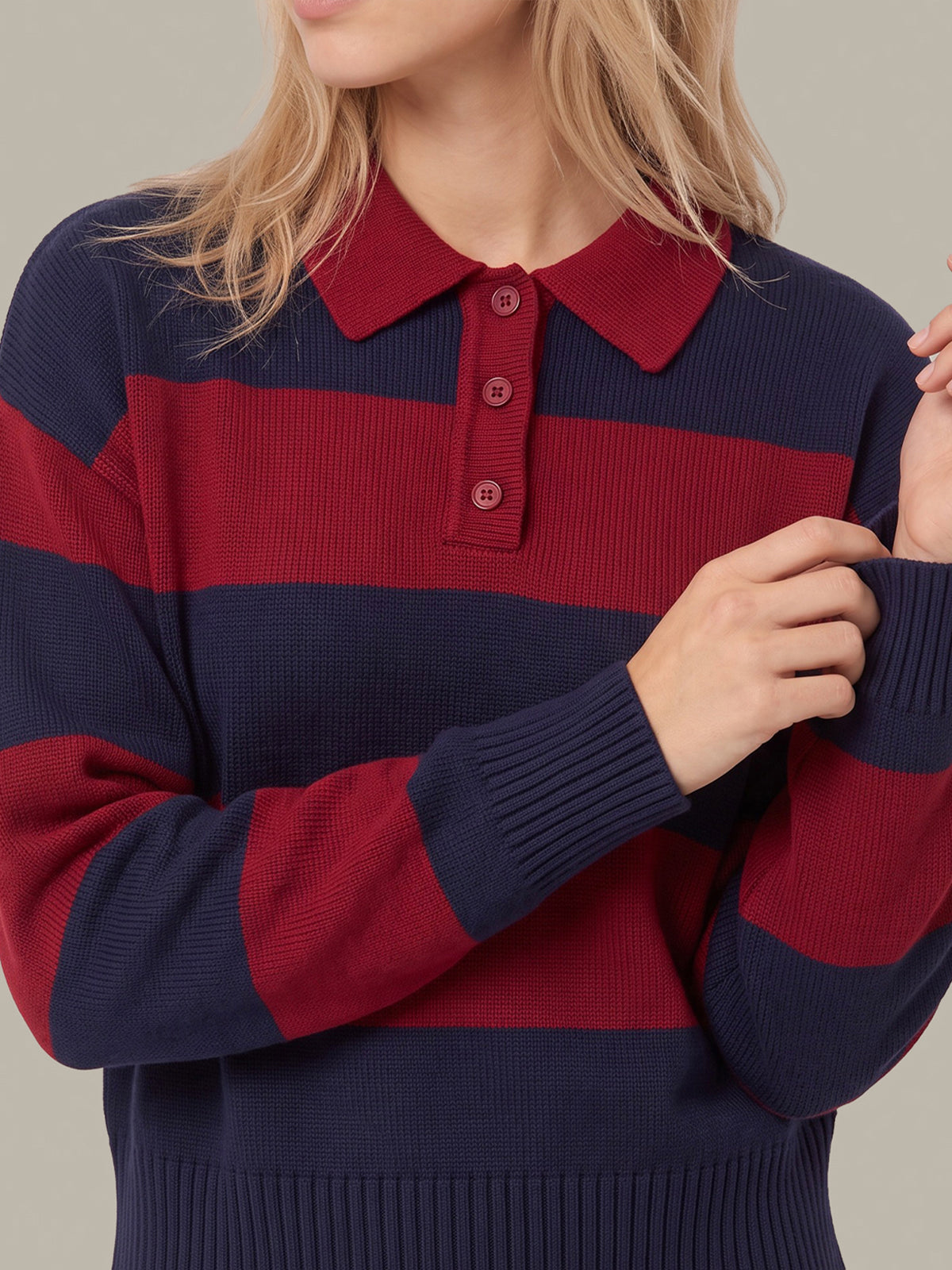 A close-up of a woman wearing a ribbed knit polo sweater with horizontal navy and burgundy stripes, featuring a three-button collar.