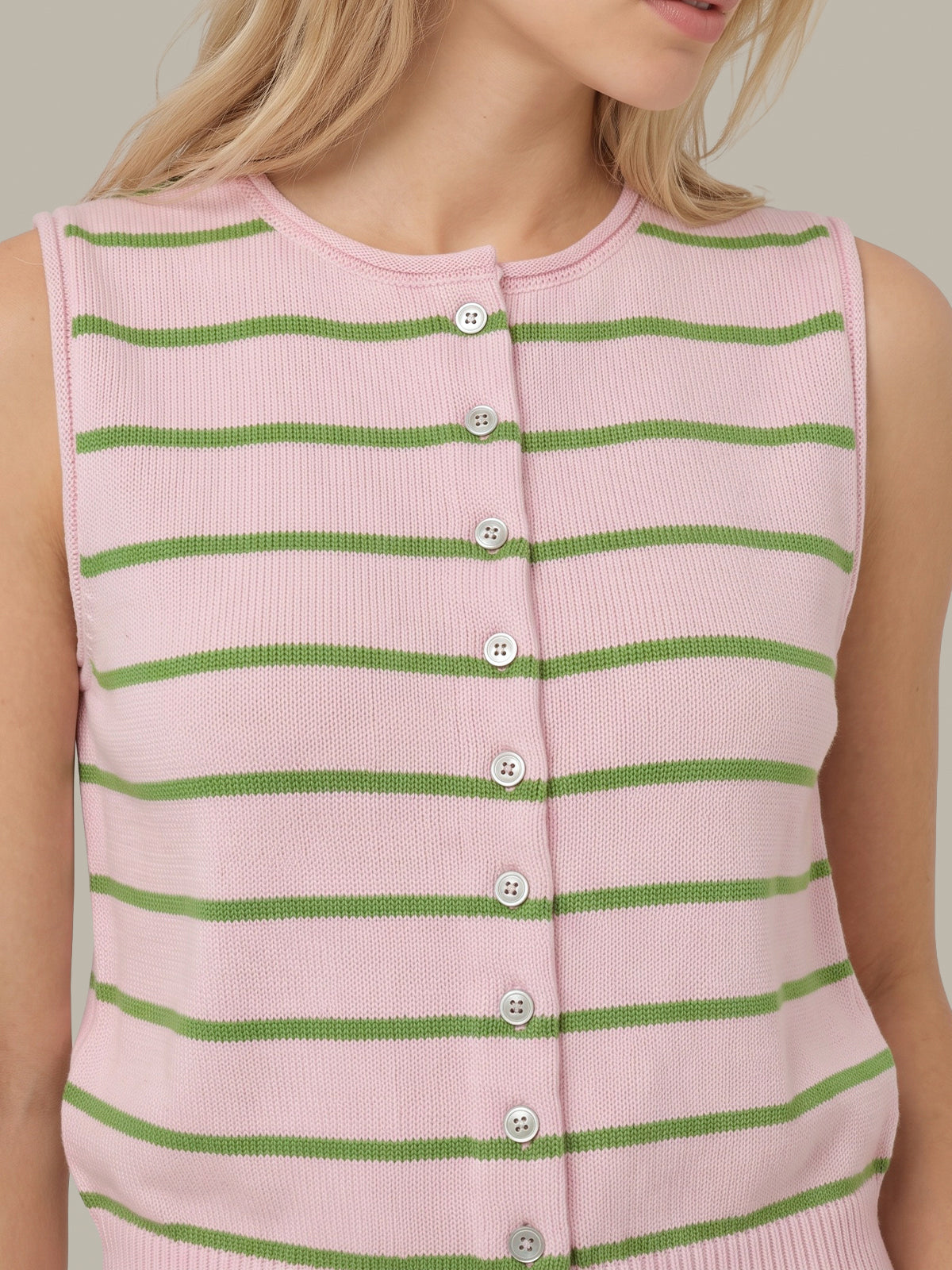 A close-up of a sleeveless ribbed knit cardigan vest with horizontal green stripes on a light pink base, featuring a button-front closure with white buttons.