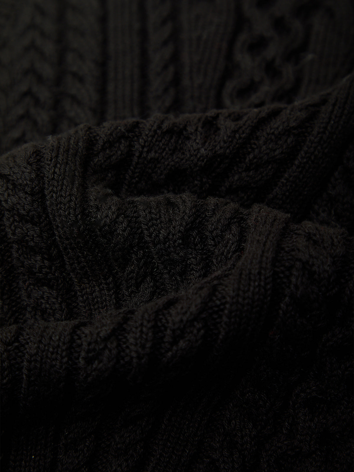 Close-up of a dark cable-knit fabric texture, showing the detailed knit pattern and folds.