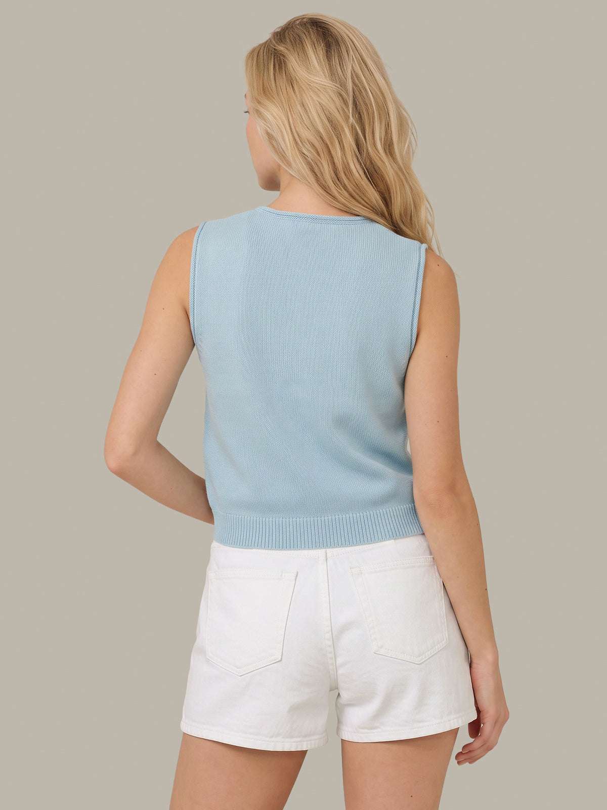 A woman shown from the back wearing a light blue sleeveless ribbed knit top and white shorts against a solid taupe background.