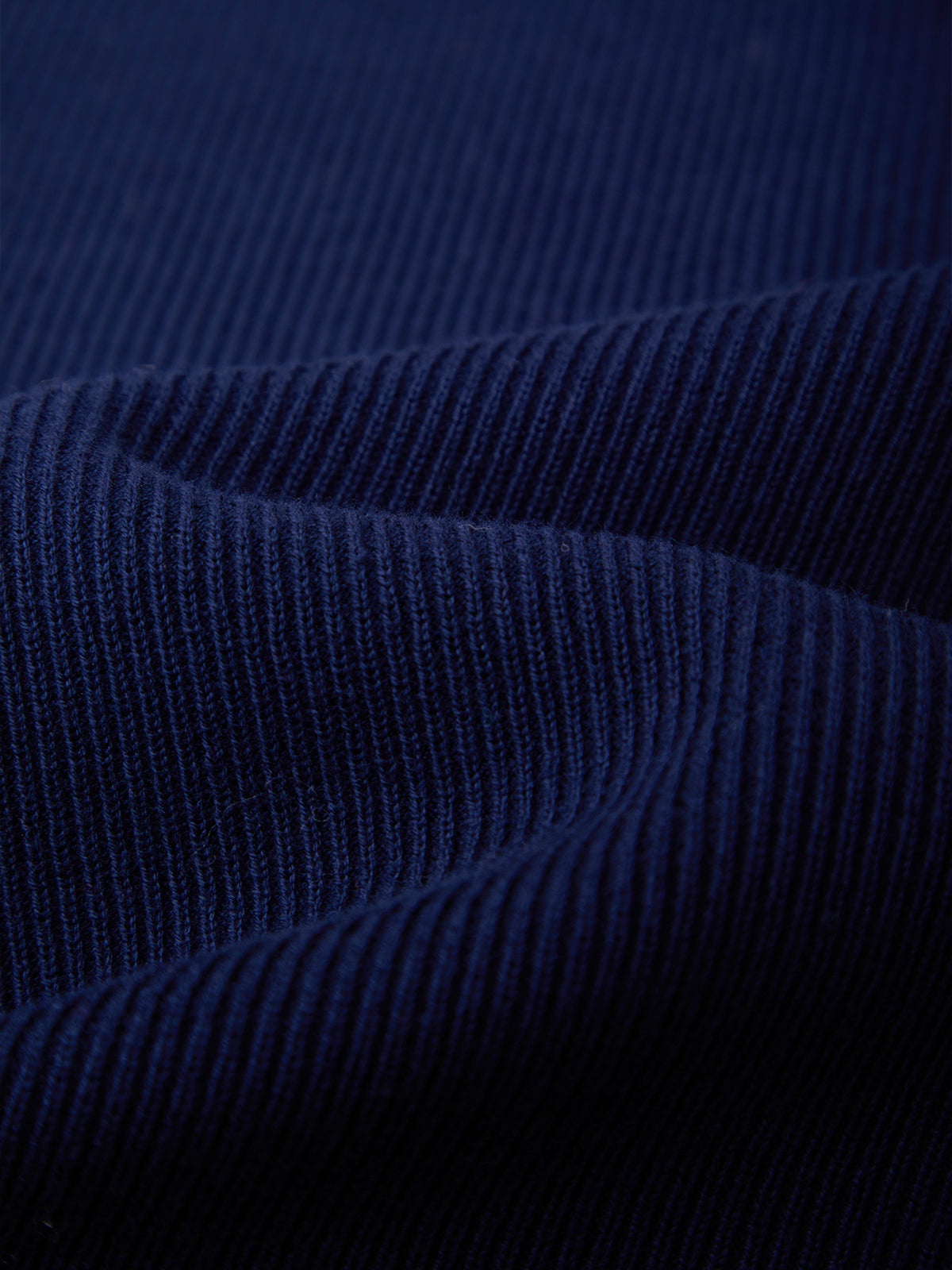 Close-up of dark navy blue ribbed fabric with a fine vertical stripe texture, showing soft folds and shadows.