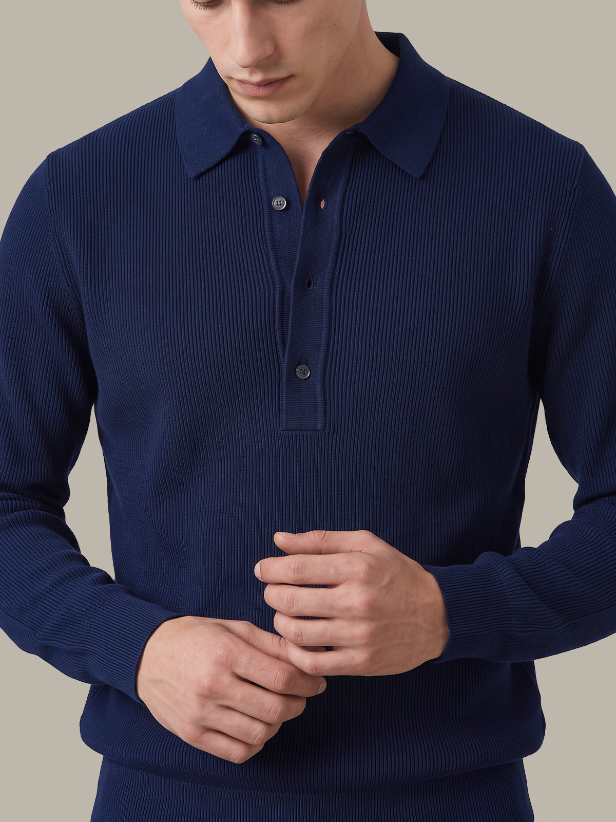 A man wearing a navy blue ribbed long-sleeve polo shirt, shown from the chest down against a plain beige background.