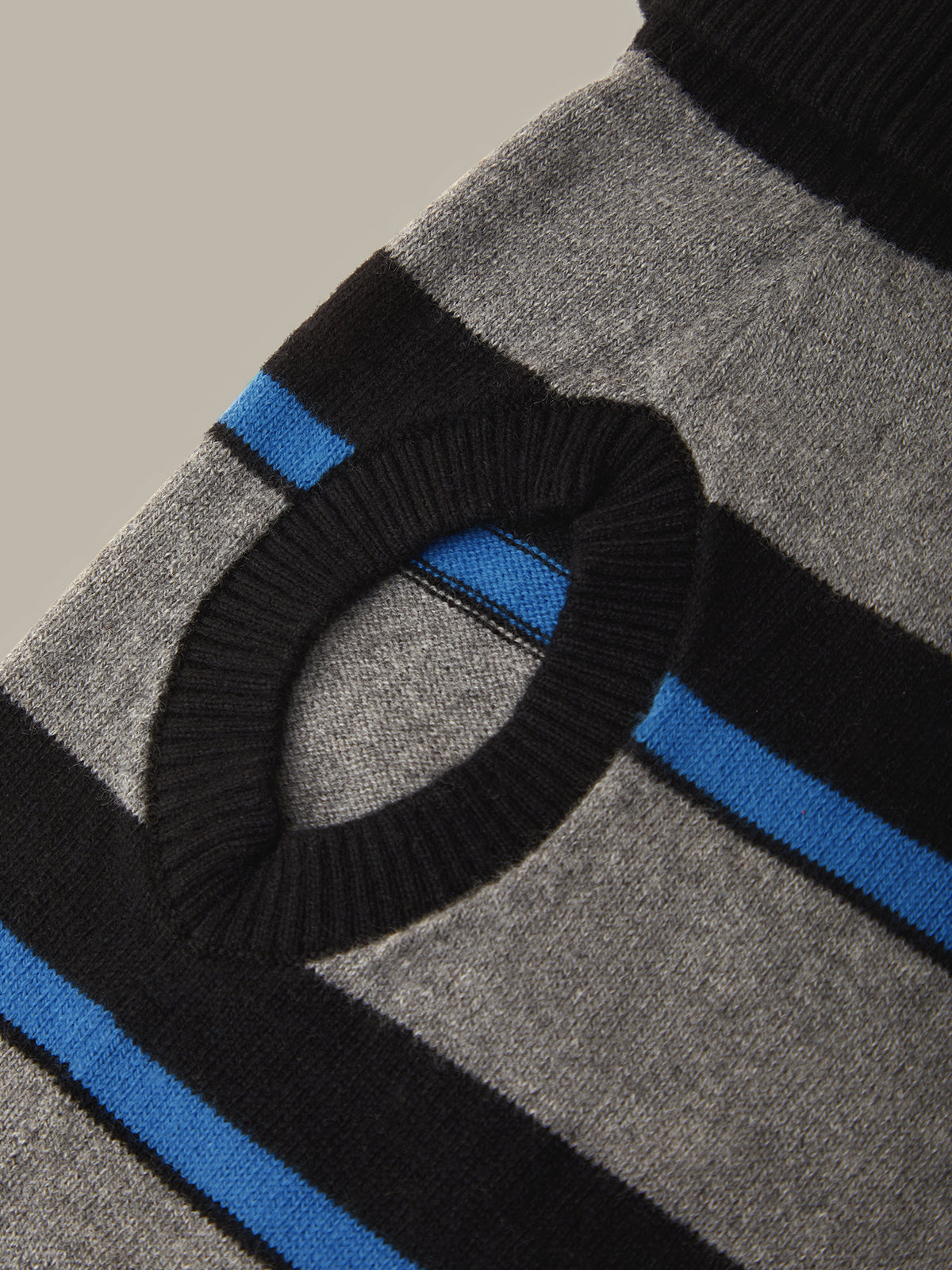 Close-up of a knit sweater featuring a gray and black striped pattern with bright blue accent stripes and a ribbed black circular knit detail.