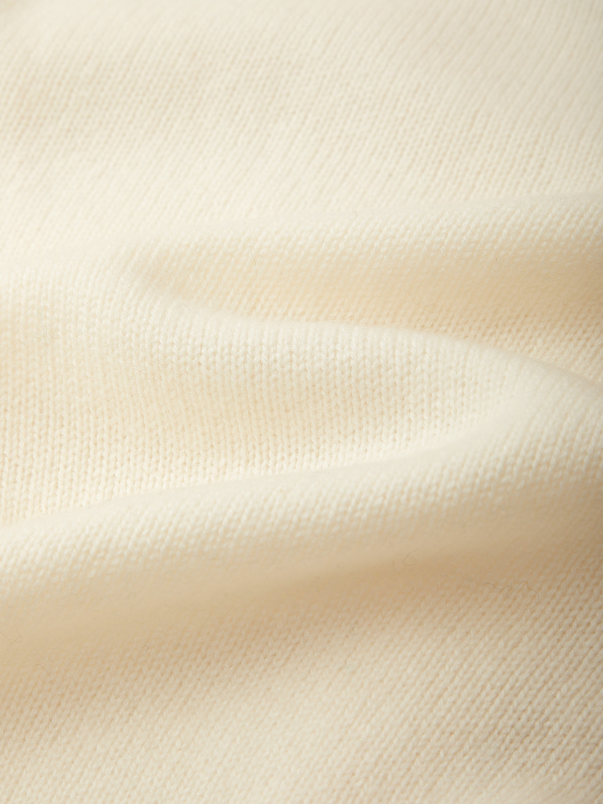 A close-up of soft cream-colored knit fabric with gentle folds and a fine ribbed texture.