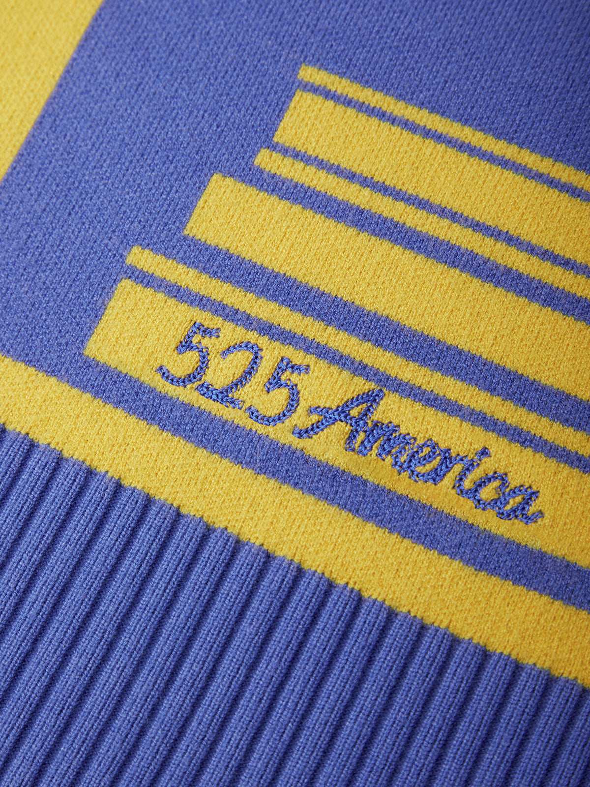 Close-up of a knit garment featuring bold yellow and blue stripes with the embroidered text '525 America' across a ribbed blue cuff.