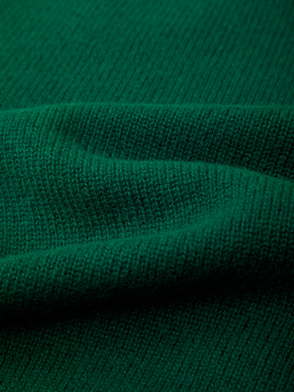 A close-up of dark green ribbed knit fabric with soft folds showing the texture and weave.