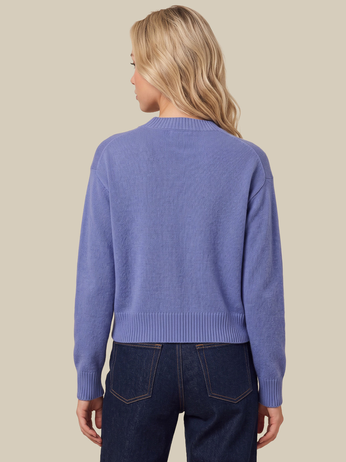 A woman shown from the back wearing a light periwinkle blue knit sweater and dark blue jeans, set against a solid beige background.