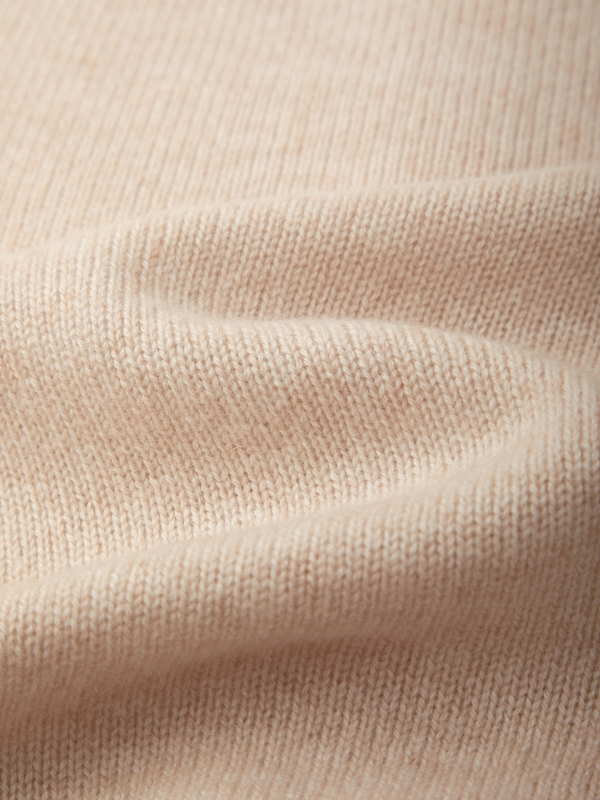 Close-up of a soft knit fabric in a pale blush pink color, showing the fine ribbed texture and gentle folds.