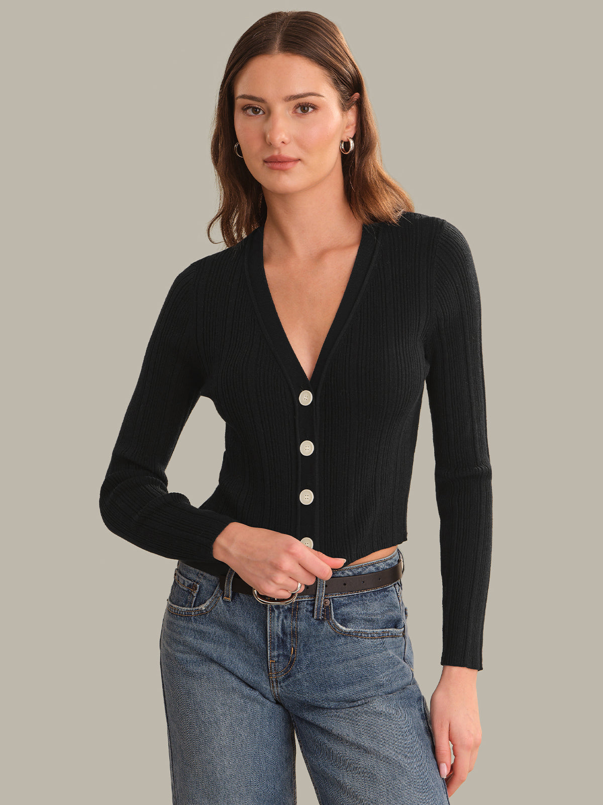 Woman wearing a black cardigan with buttons and blue jeans on a gray background