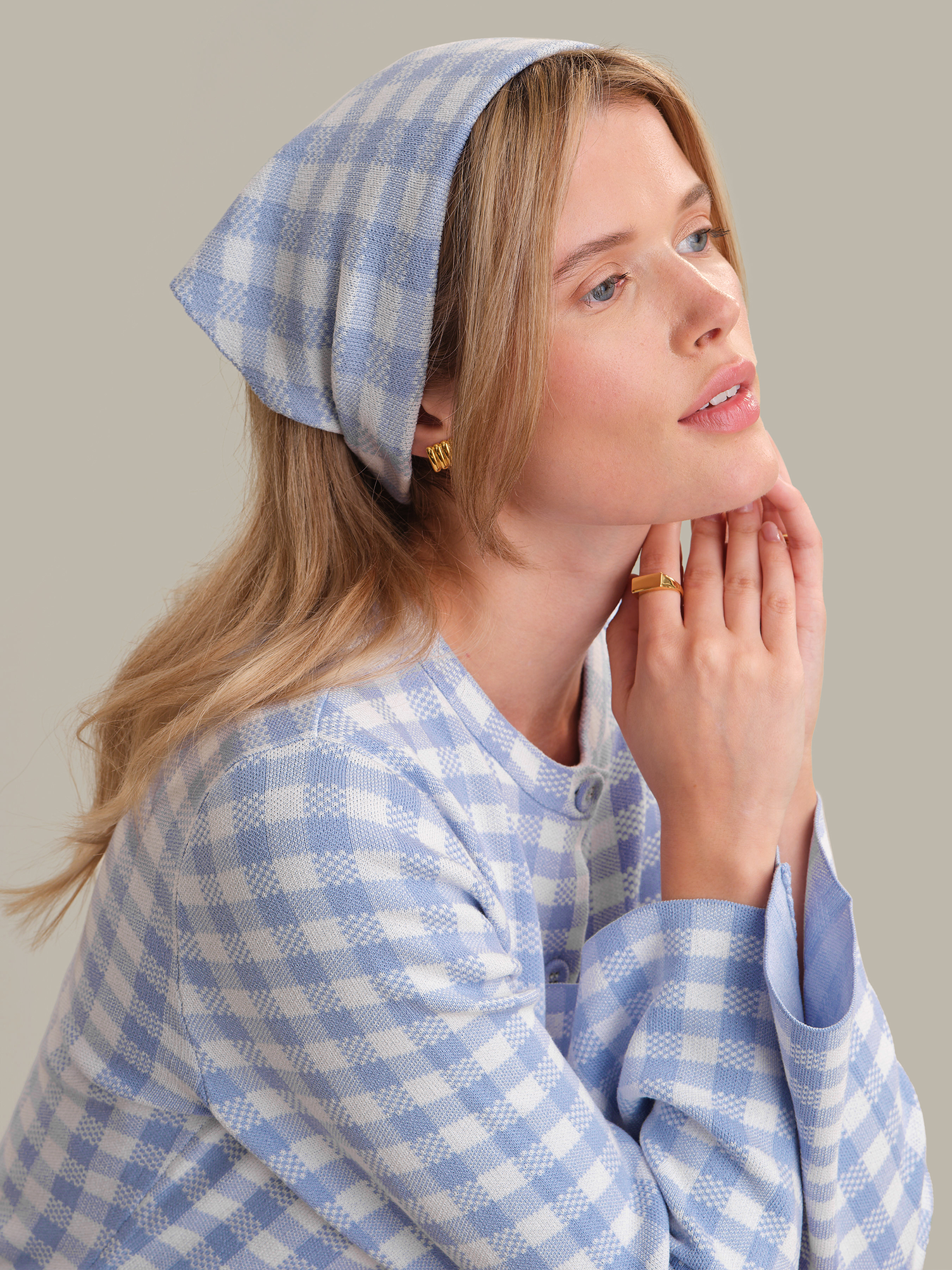 Woman wearing a blue and white checkered headscarf and robe against a neutral background