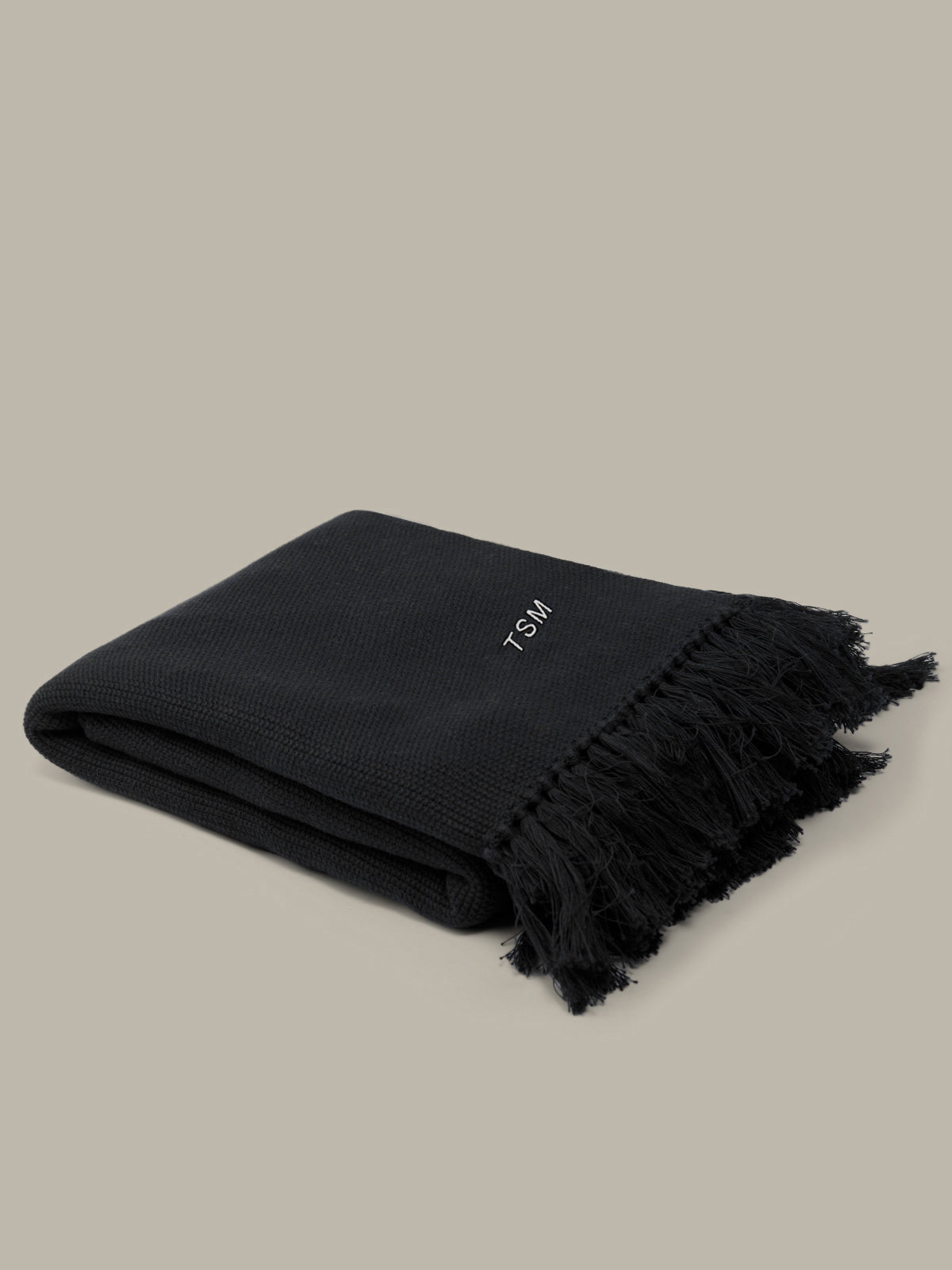 Black blanket with frayed edges on a beige background
